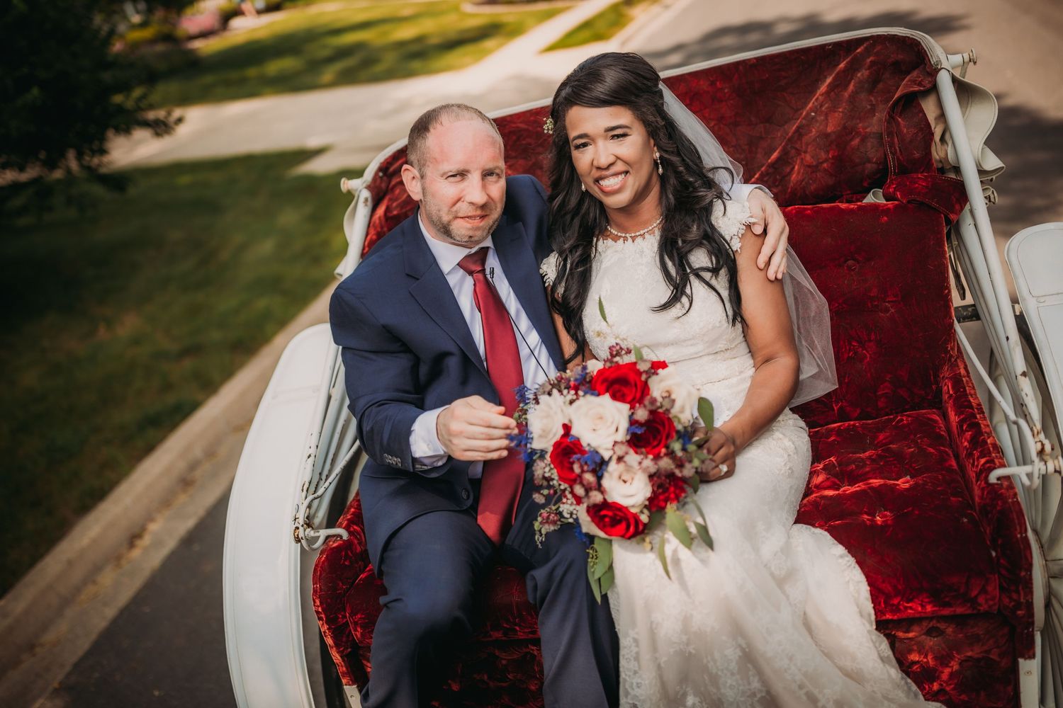 Newlyweds share laughter while seated in an ornate white carriage with red interior.