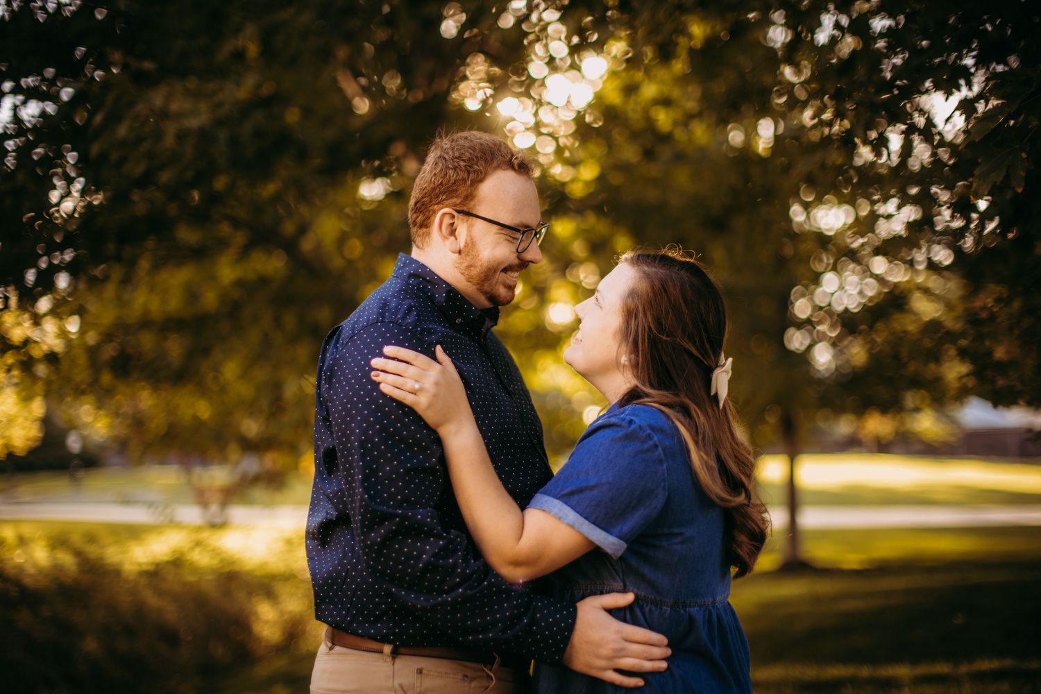 Couple embracing outdoors during sunset with golden bokeh lighting.