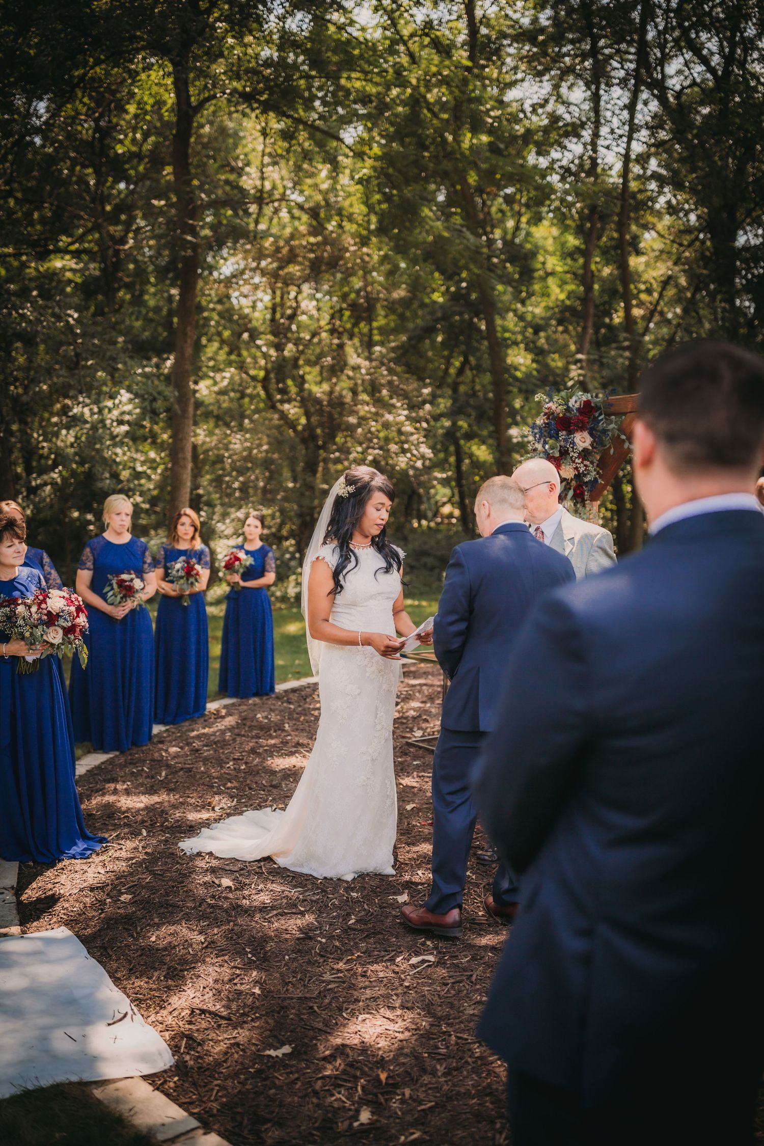 Wedding party gathered in a wooded outdoor setting with guests in navy blue attire.