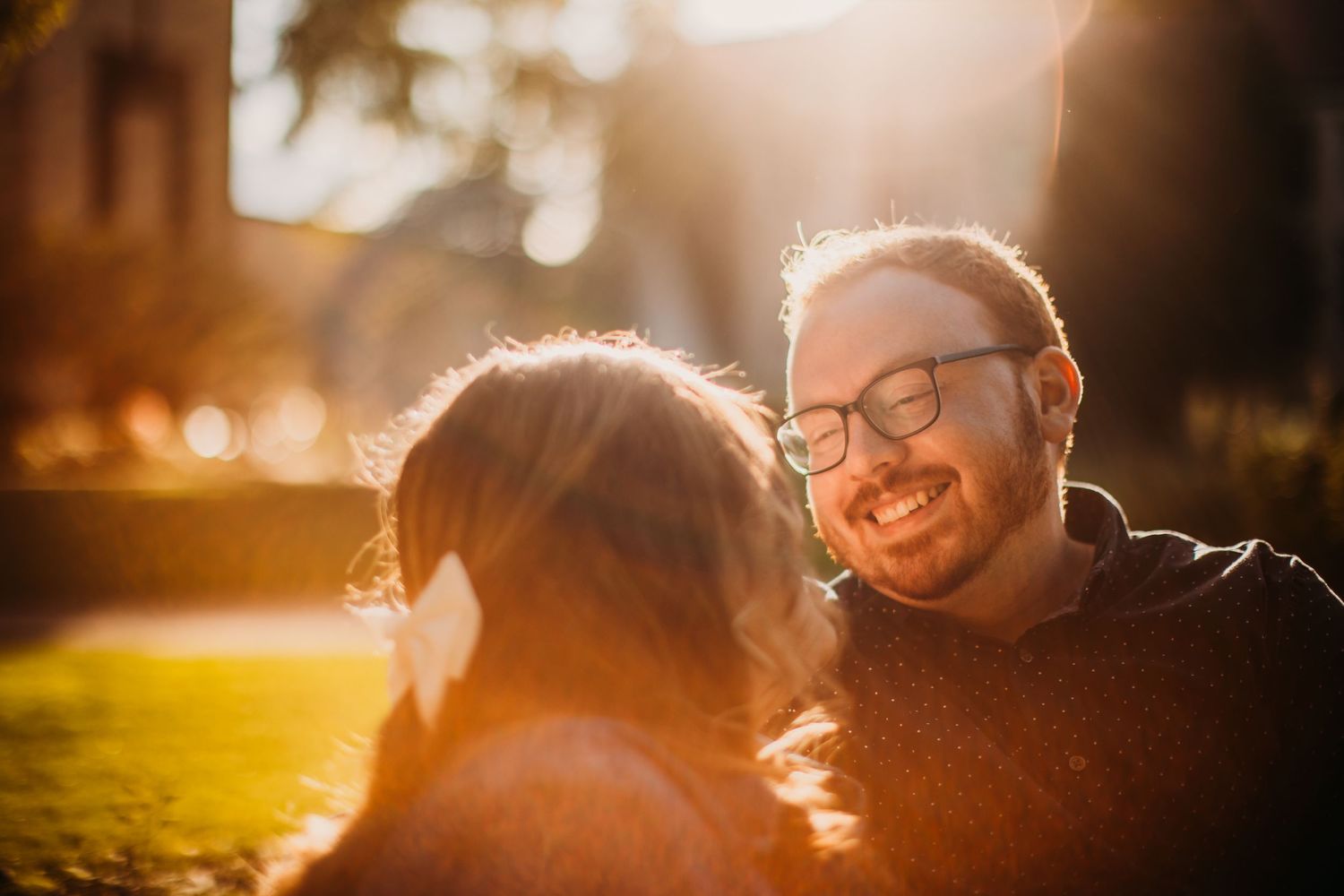 A couple laughs together in warm sunset lighting surrounded by golden bokeh.