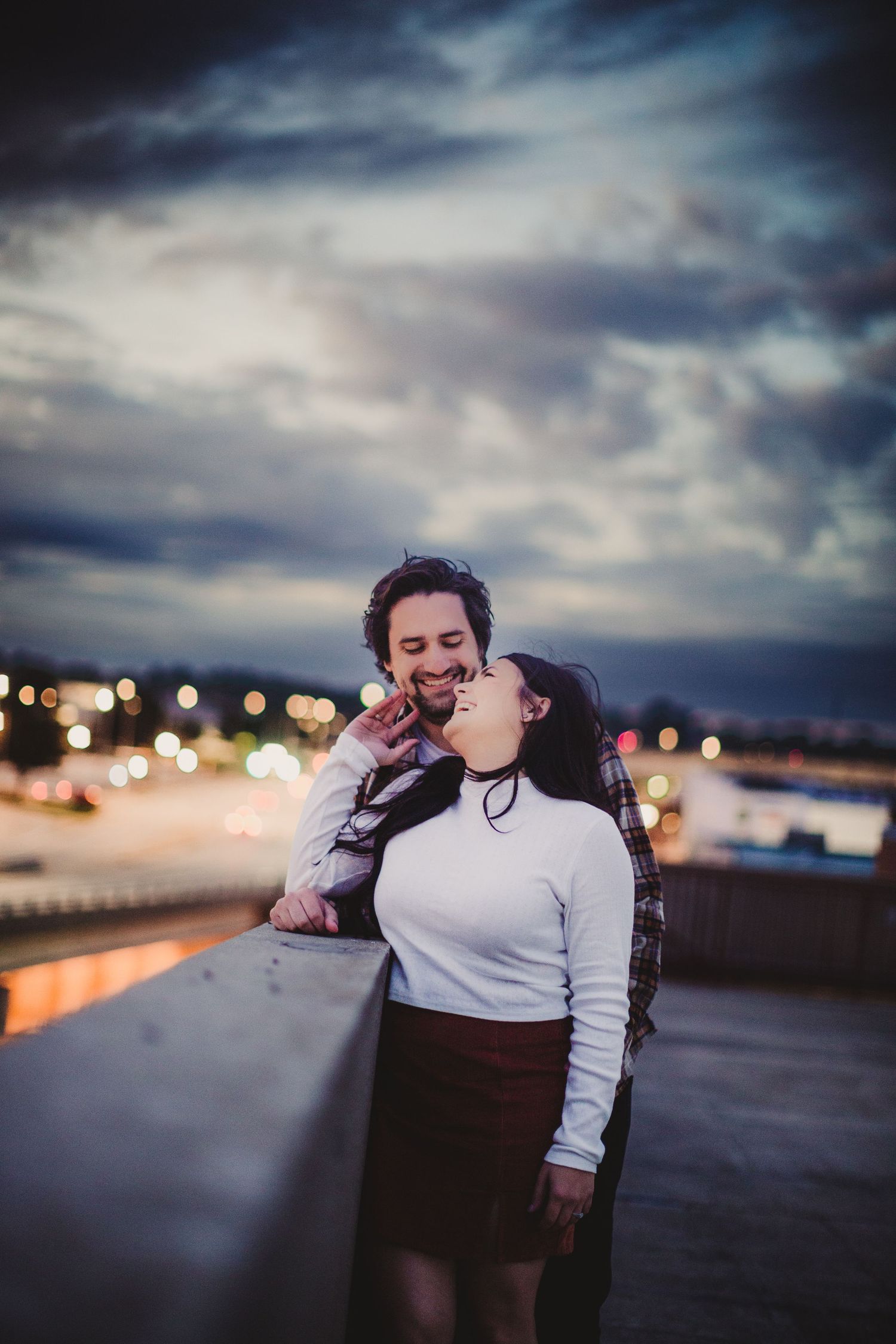 A couple shares laughter while leaning against a railing during twilight.