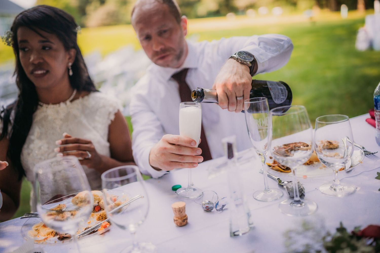 Wedding reception table setting with white linens and celebratory drinks in an outdoor setting.