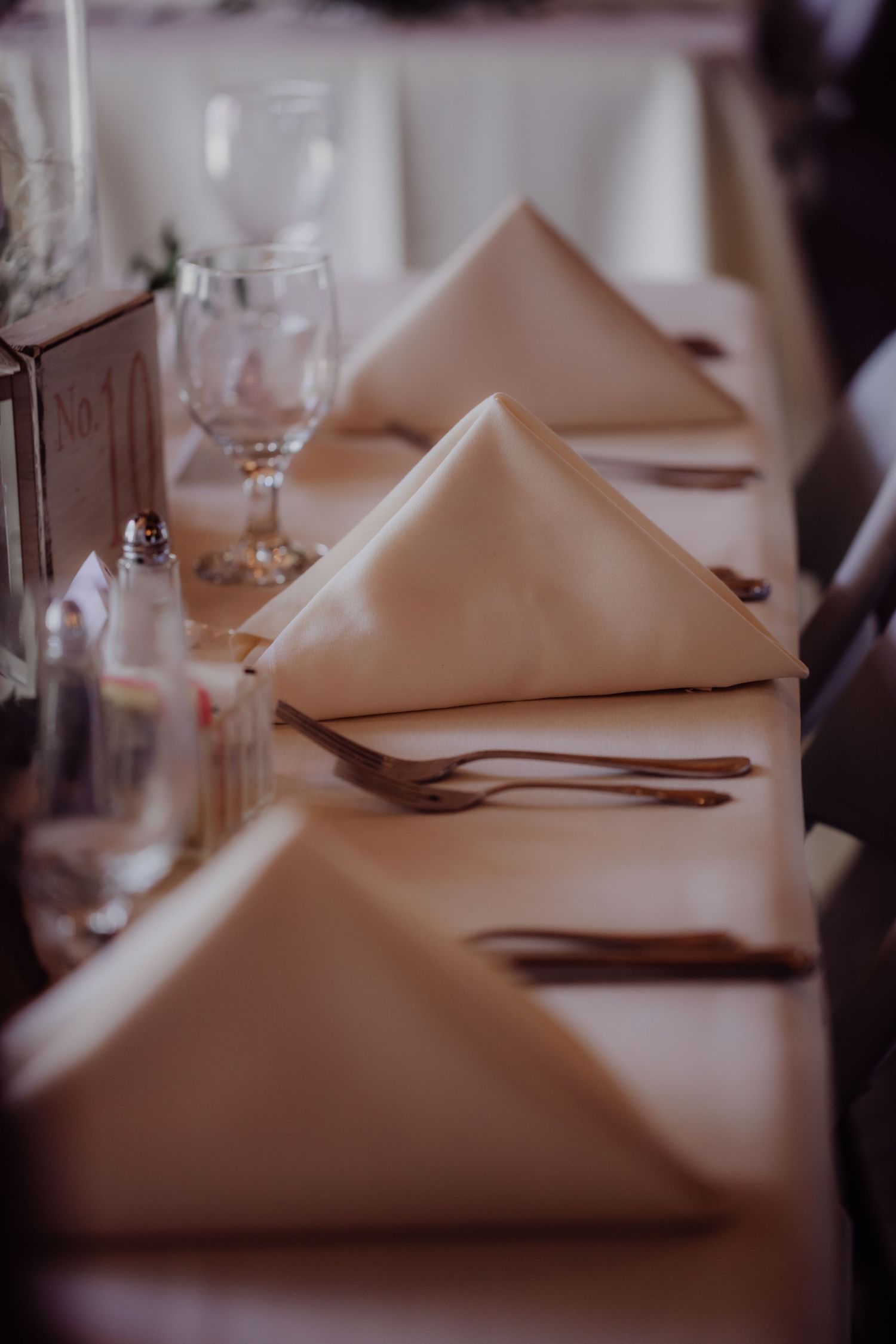 Close-up of formal place settings with folded napkins and wine glasses on white tablecloths.