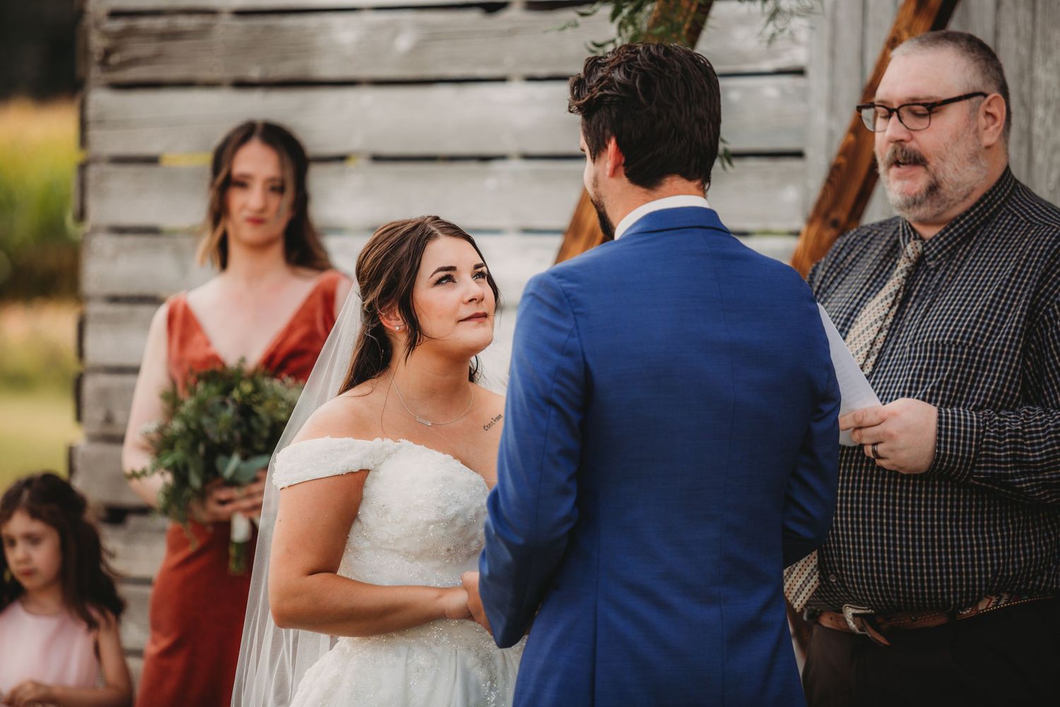 Intimate outdoor wedding ceremony with rustic barn backdrop and white and blue attire.