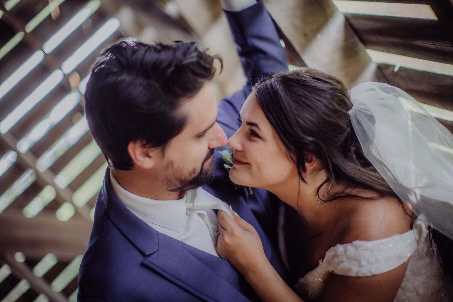 Intimate portrait of bride and groom touching foreheads against geometric wooden backdrop.