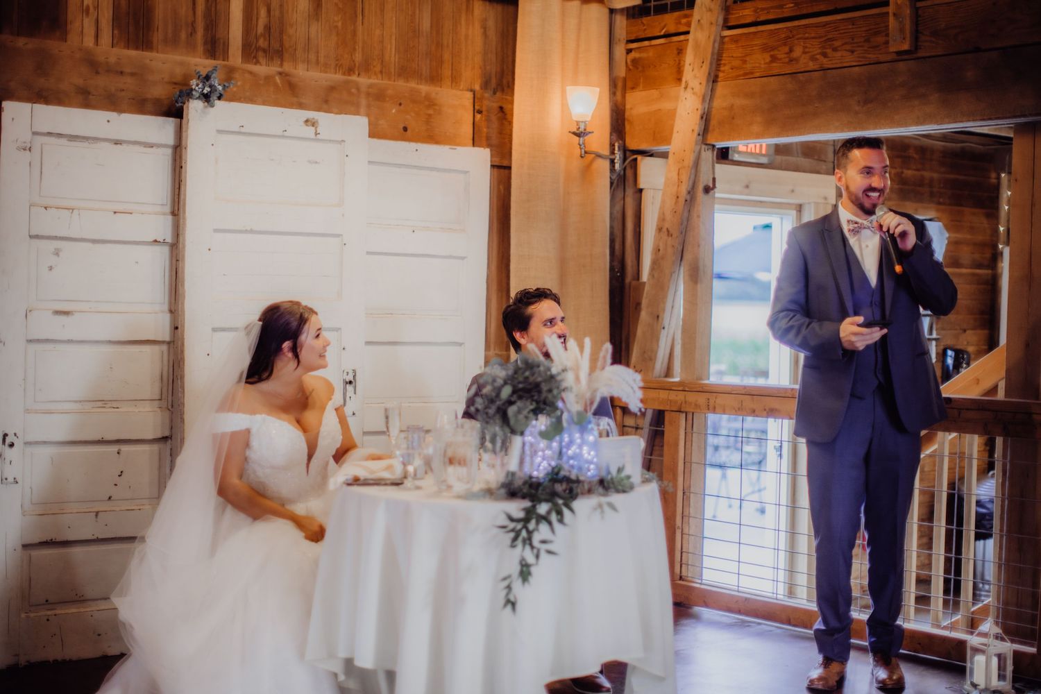 Wedding speeches and toasts during reception in rustic barn setting with white walls.