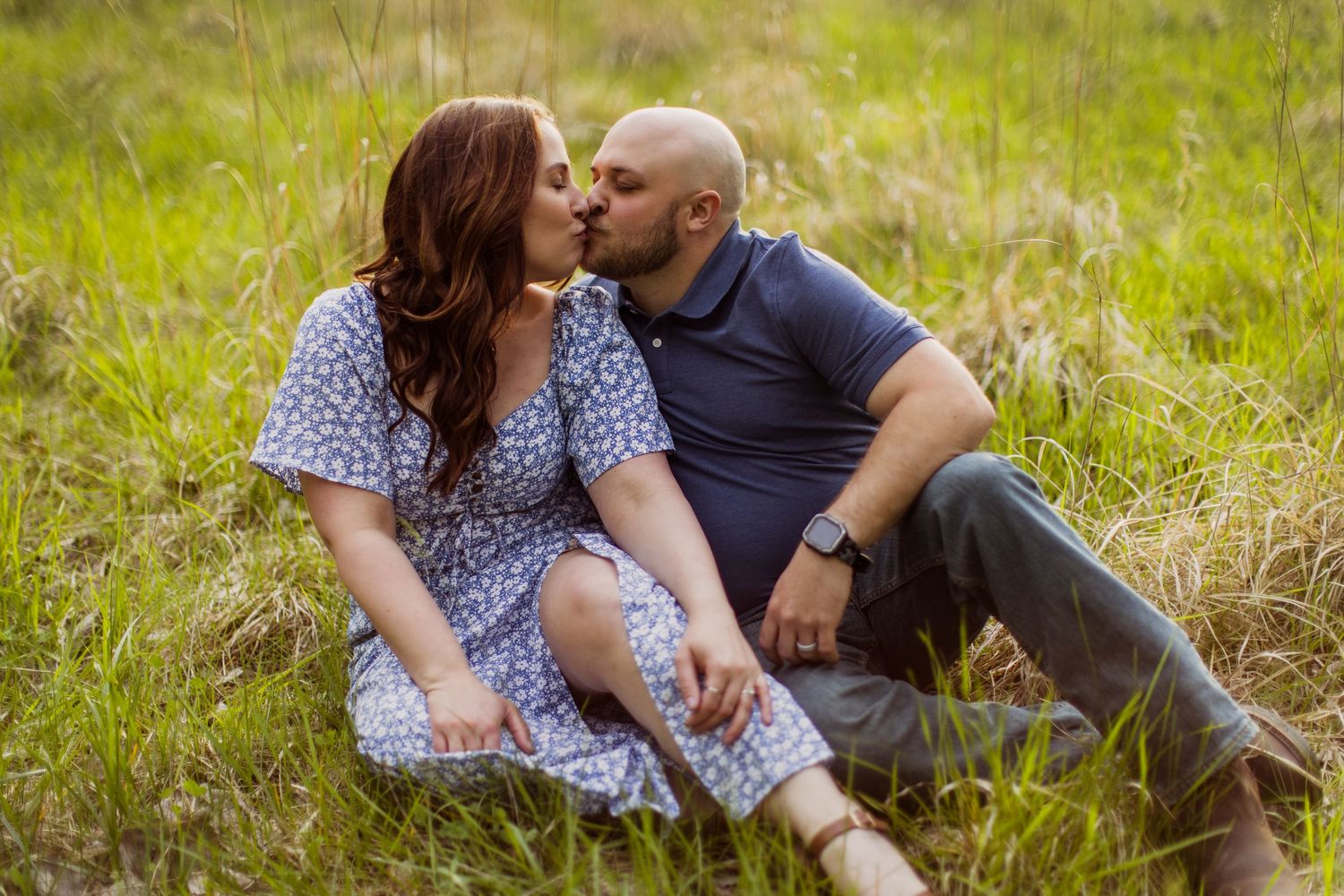 A tender moment between a couple sitting in a sun-lit meadow during their photo session.