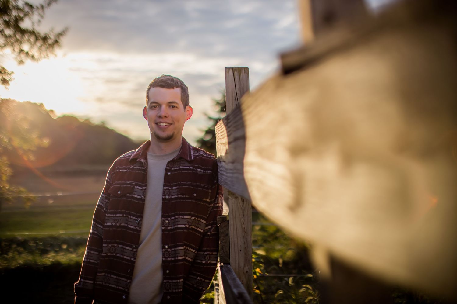 Portrait of man in patterned shirt with golden sunlight and fence in background.