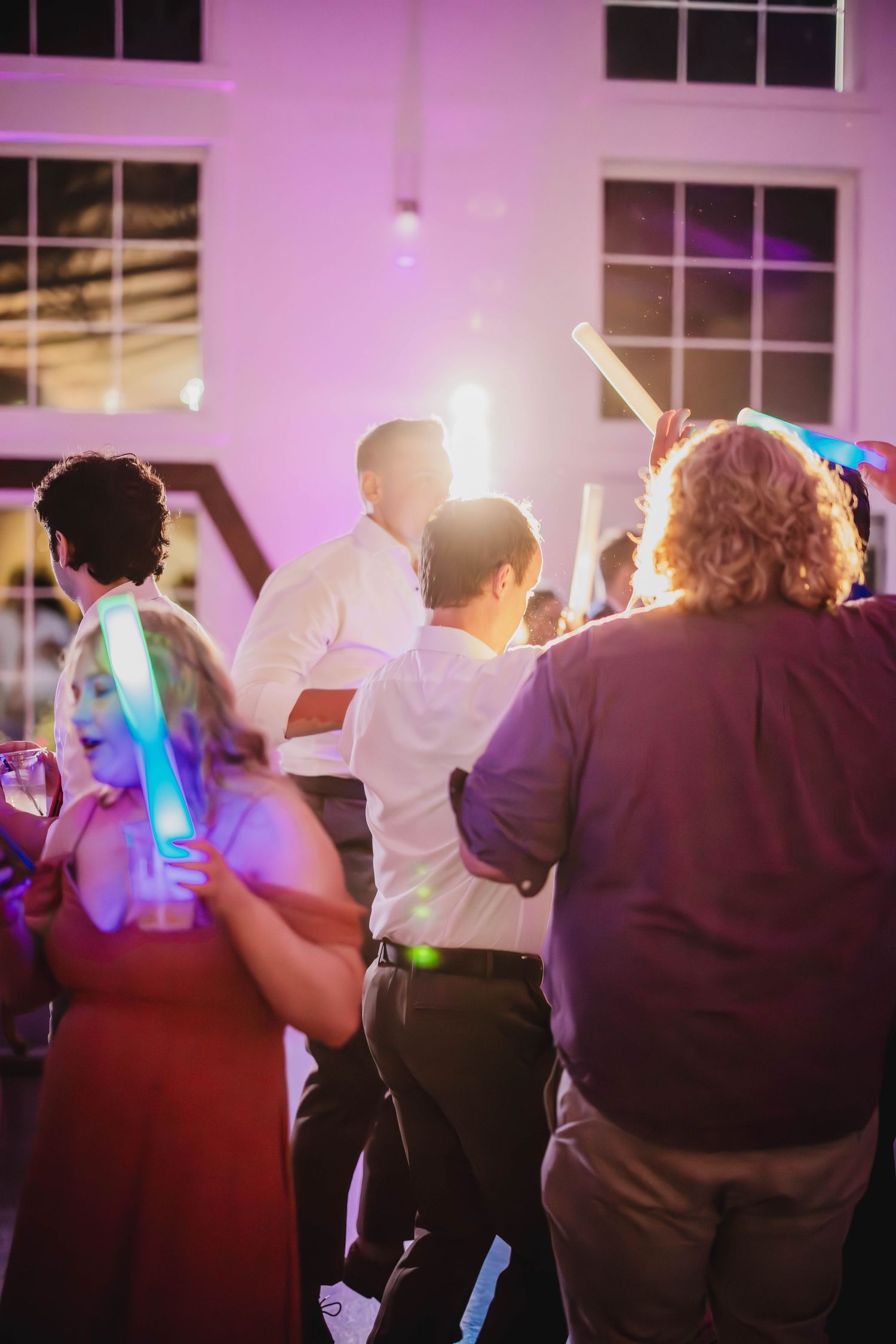 Party guests dancing with glowing LED sticks under atmospheric purple lighting.
