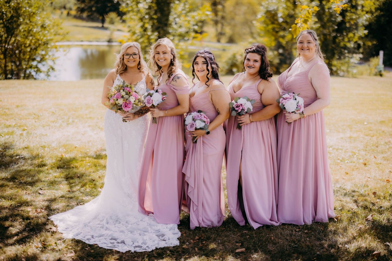 Bridesmaids in pink dresses hold floral bouquets while posing outdoors.