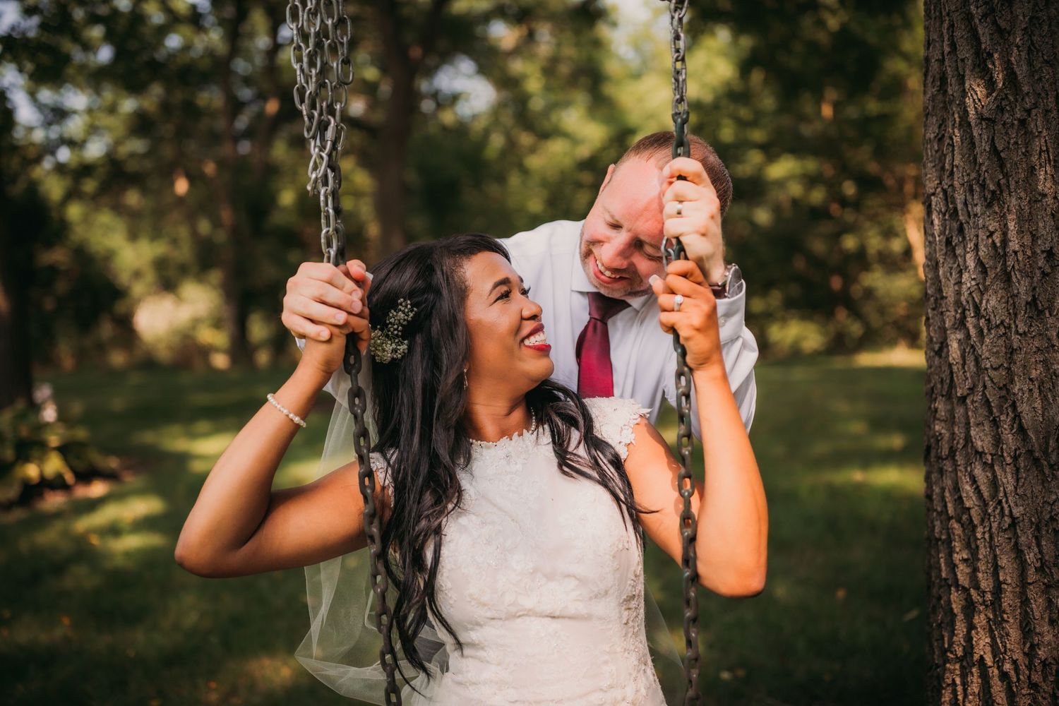 Wedding couple shares joyful moments on a rustic tree swing in a park.