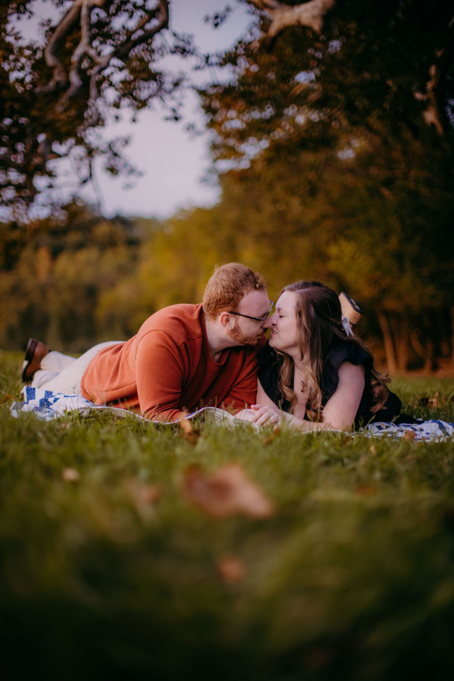 Intimate moment between couple lying on blanket in golden autumn setting.