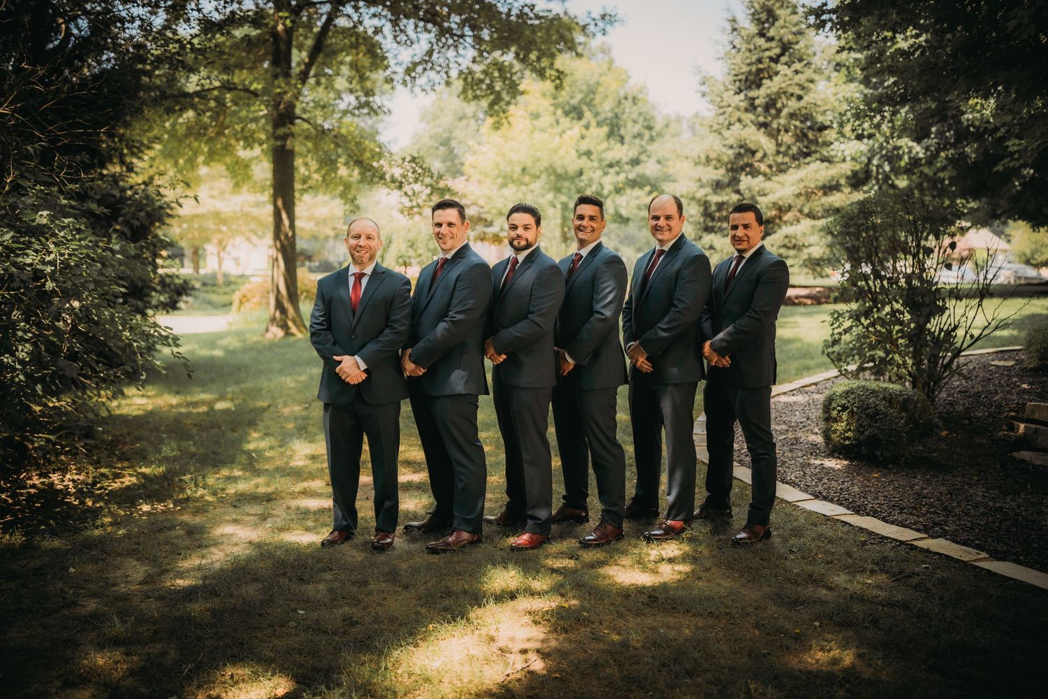 Wedding party poses for formal photos in a natural outdoor setting with golden sunlight.
