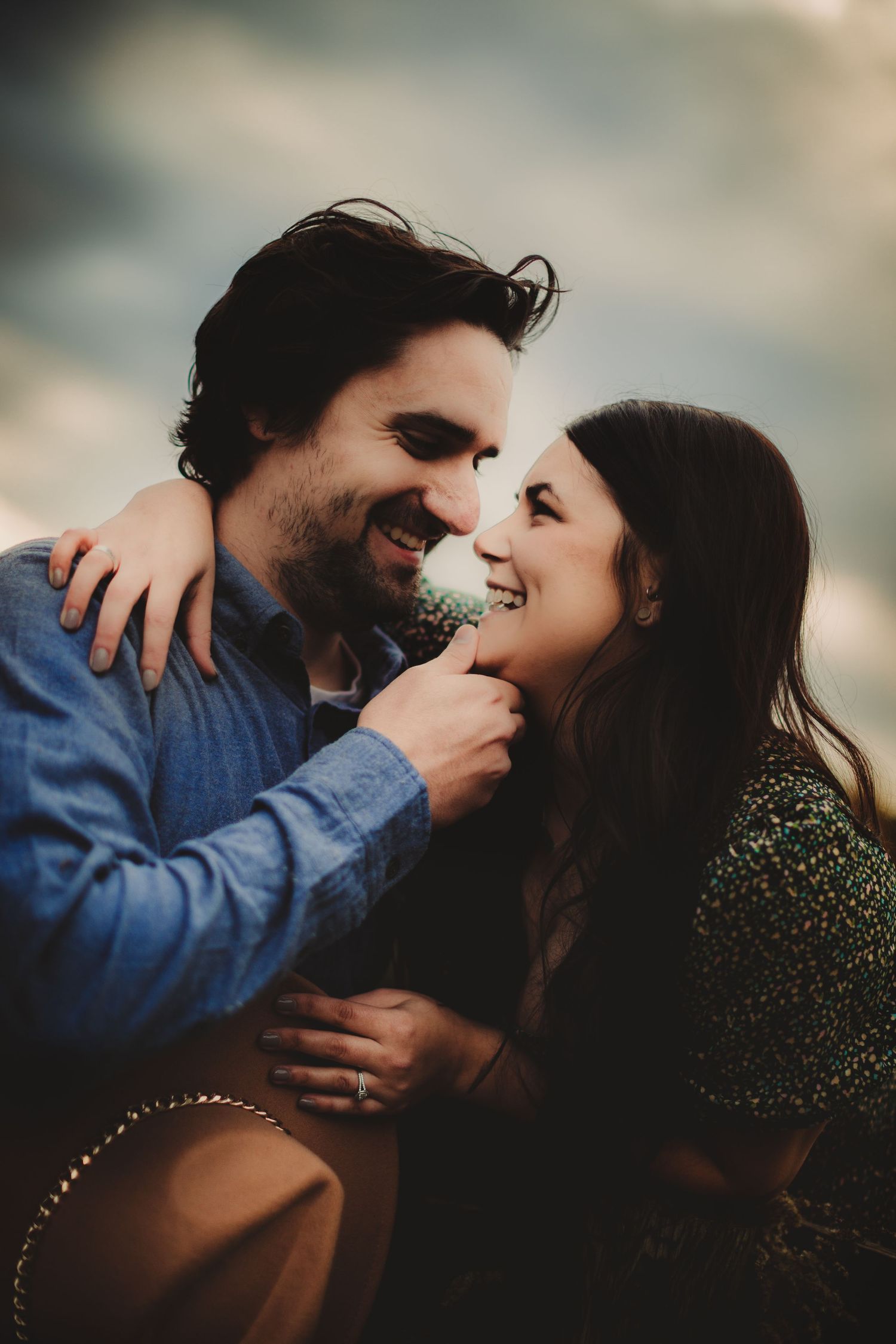 Intimate portrait of couple sharing laughter and tender touches against blurred background.