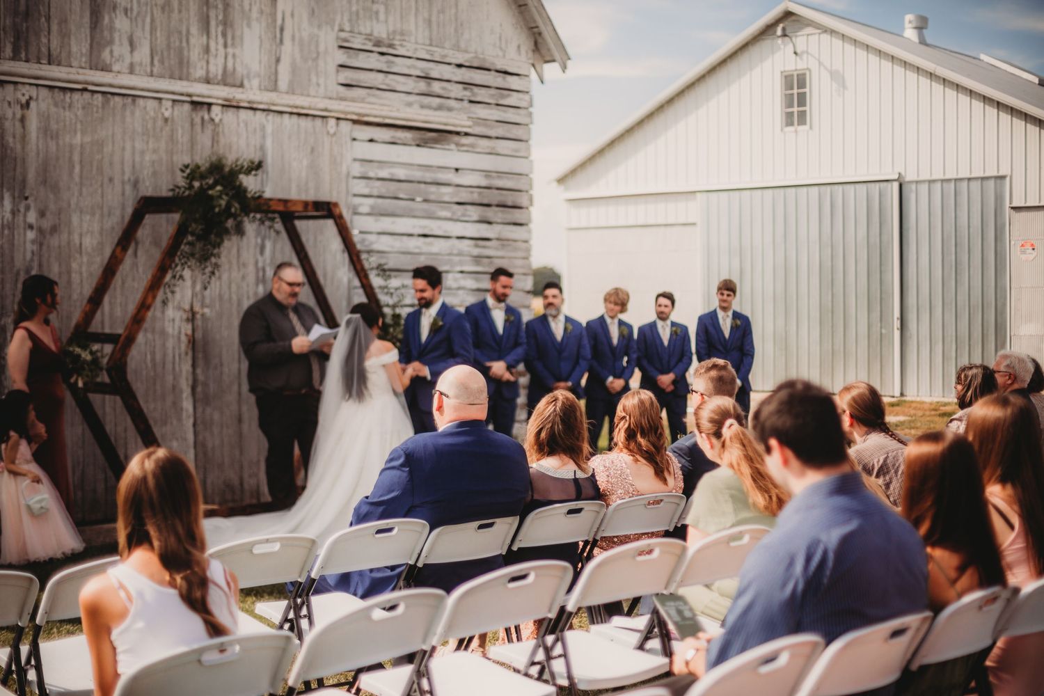 Wedding ceremony in progress with wooden hexagon arch against rustic barn backdrop.
