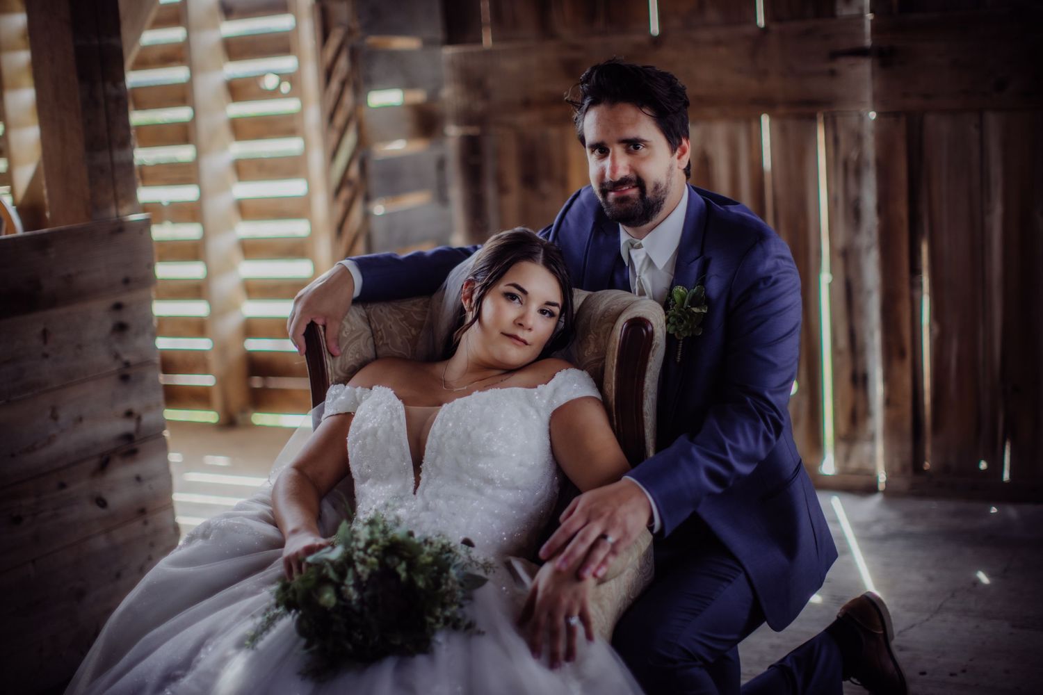 Elegant wedding moment captured in a wooden barn with streaming light creating dramatic shadows.