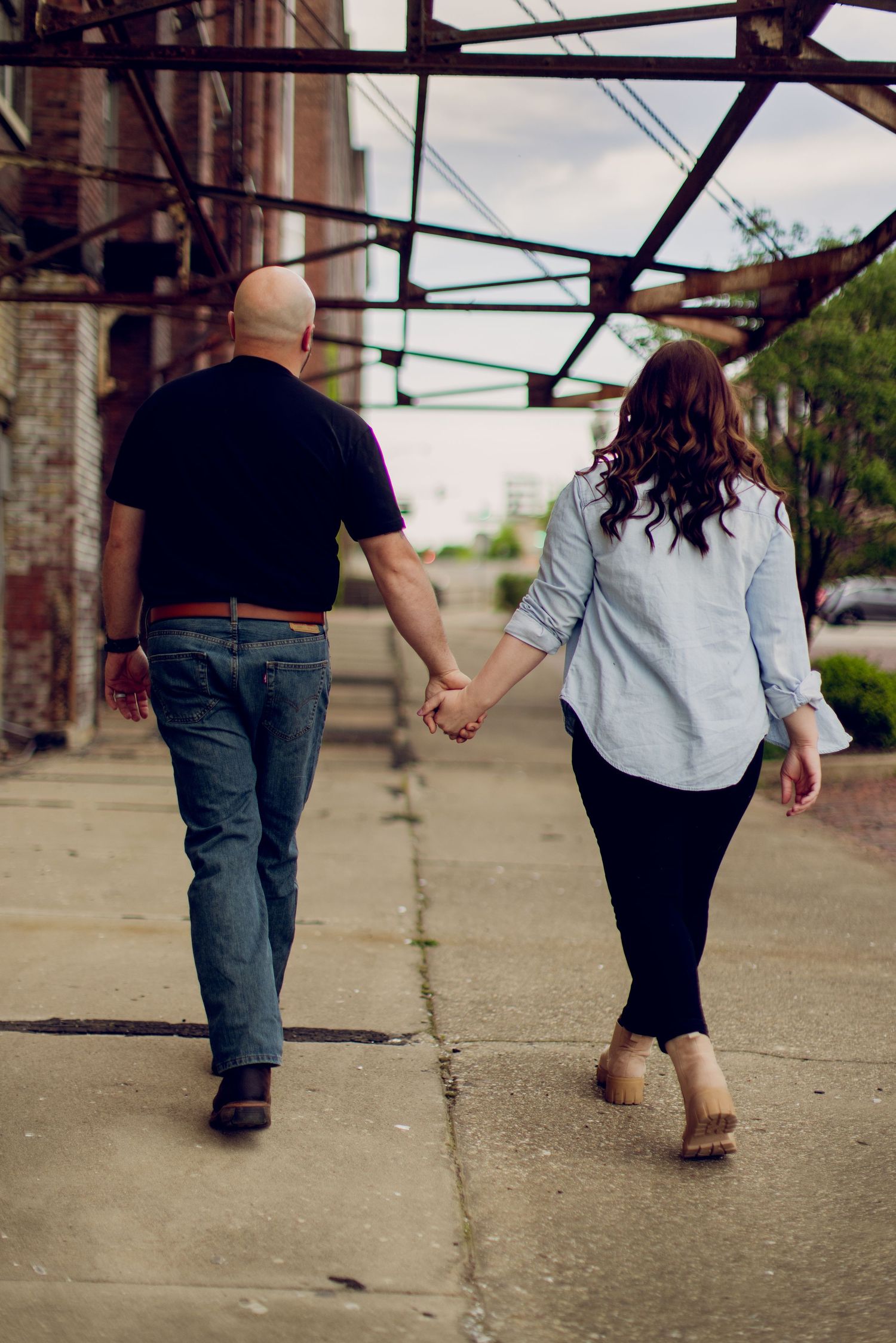 A black and white portrait of a couple embracing against a wall covered in ivy.