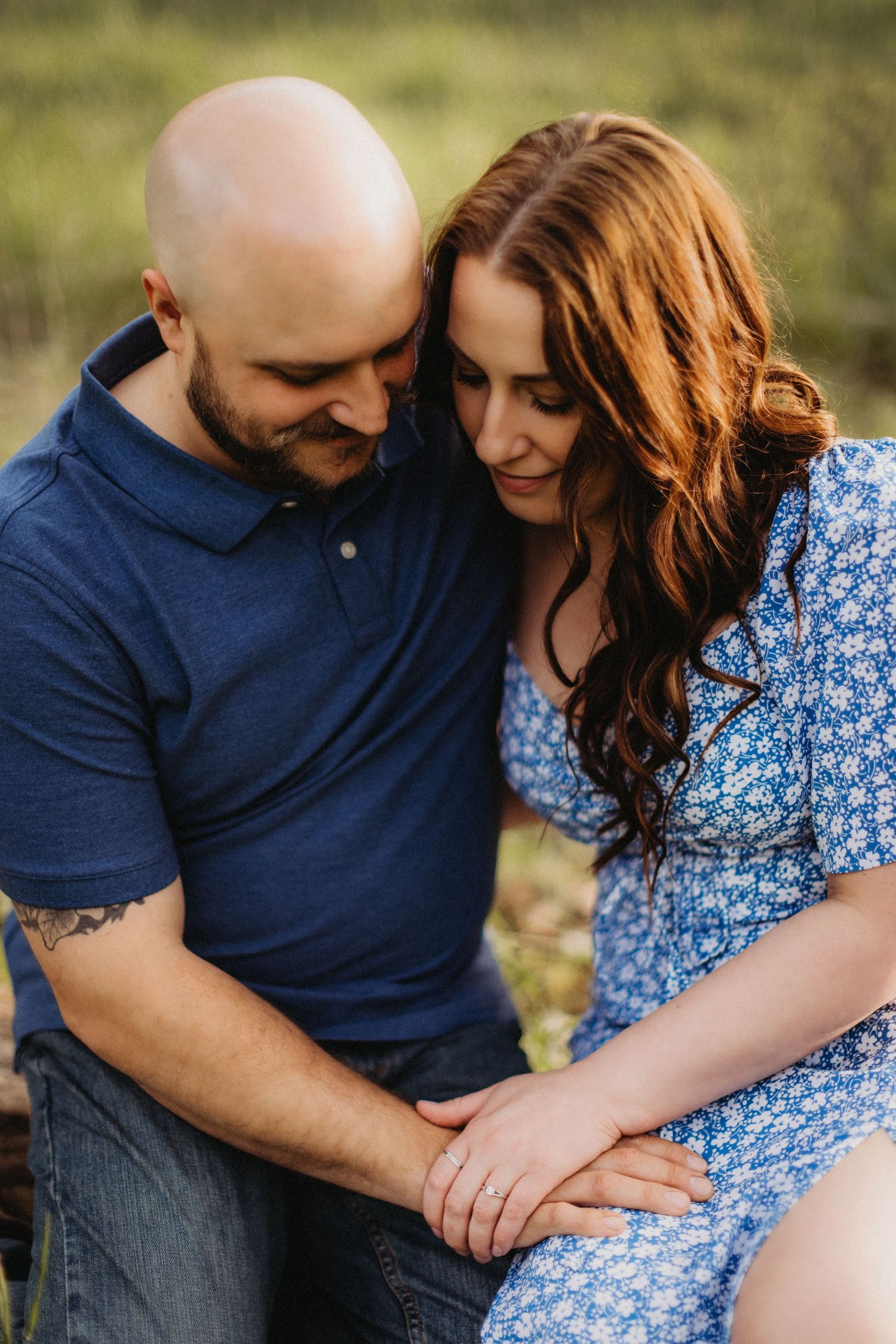A close-up outdoor portrait of a couple in casual attire showing affection while sitting together.