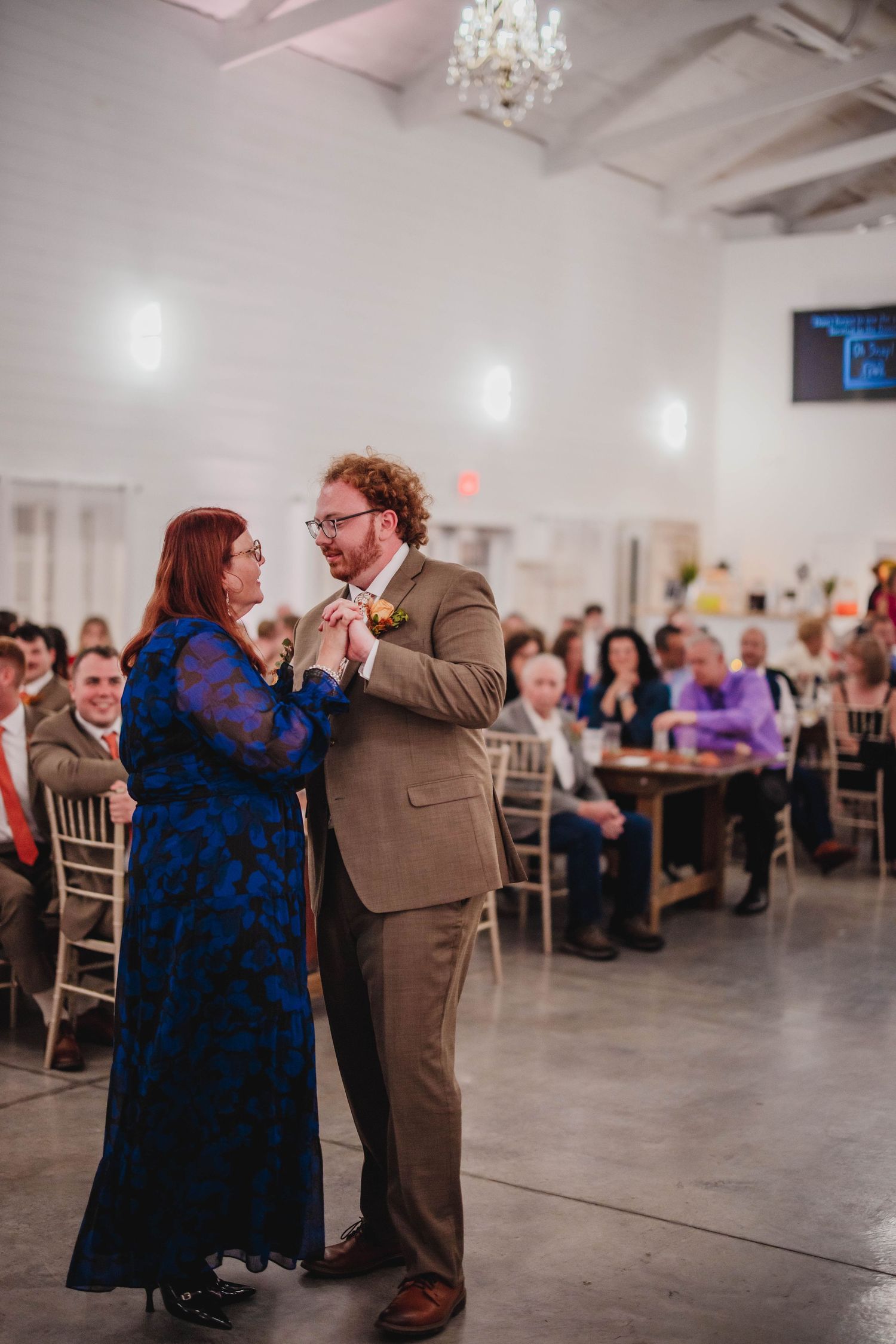 A couple sharing a romantic dance moment at a wedding reception surrounded by seated guests.