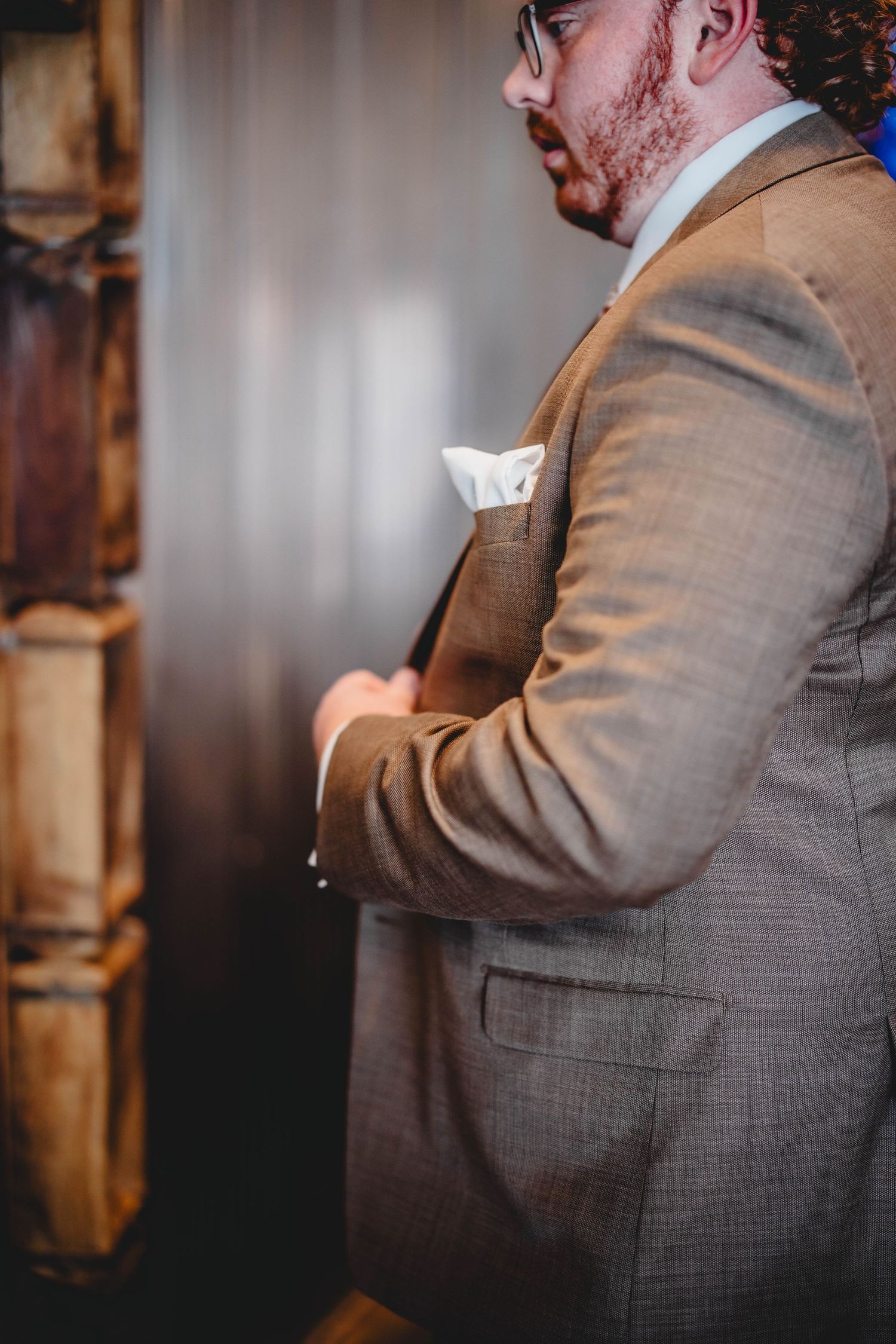Side profile of someone in a brown suit jacket adjusting their formal attire.