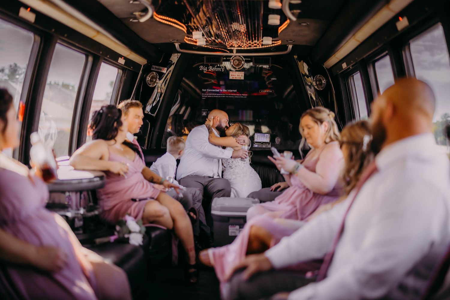 Party bus interior filled with wedding guests in coordinated pink and white attire.