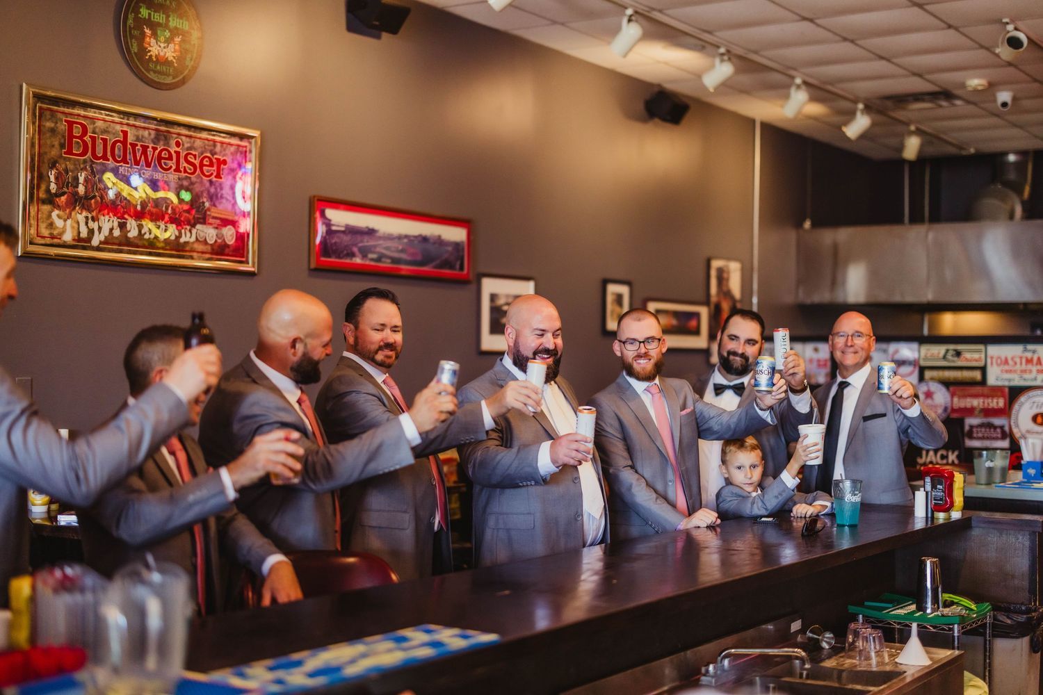 Groomsmen gather at a bar counter sharing drinks and laughter during pre-wedding celebrations.