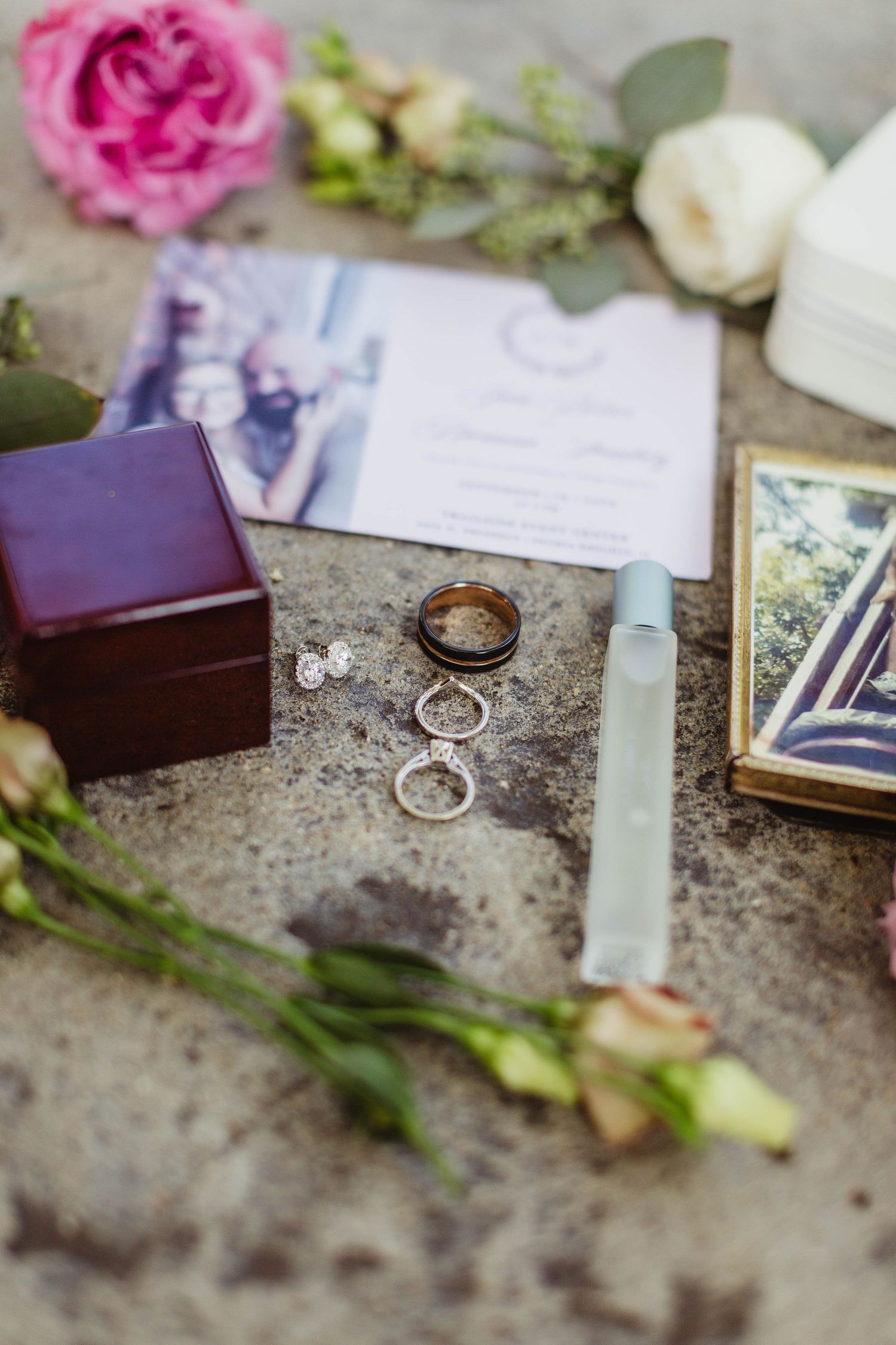 Wedding rings and invitation styled with pink roses and vintage decorative elements.
