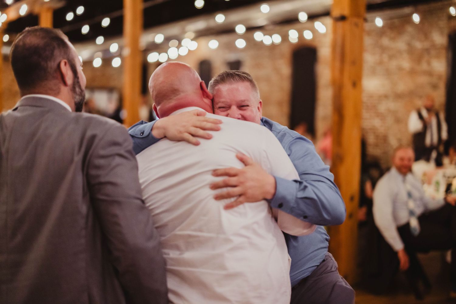 Wedding guests embrace while dancing under warm lighting in a rustic wooden barn venue.