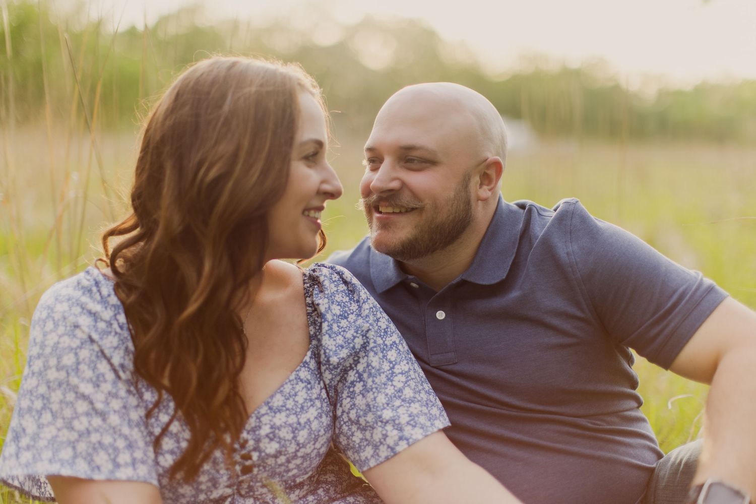 A couple shares genuine laughter during their sunset portrait session in a field.