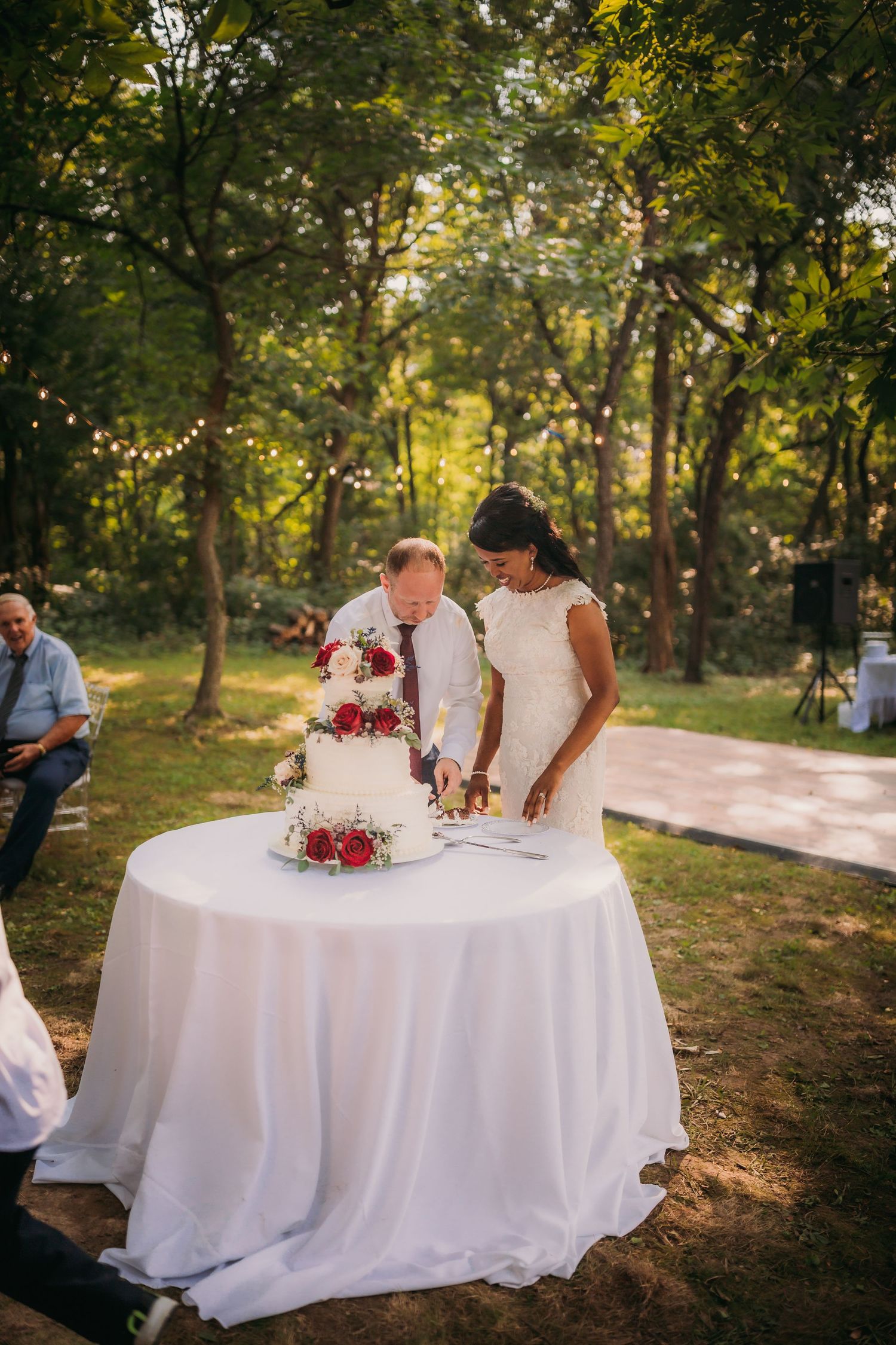 Wedding ceremony document signing at a white-clothed table in a wooded outdoor setting.