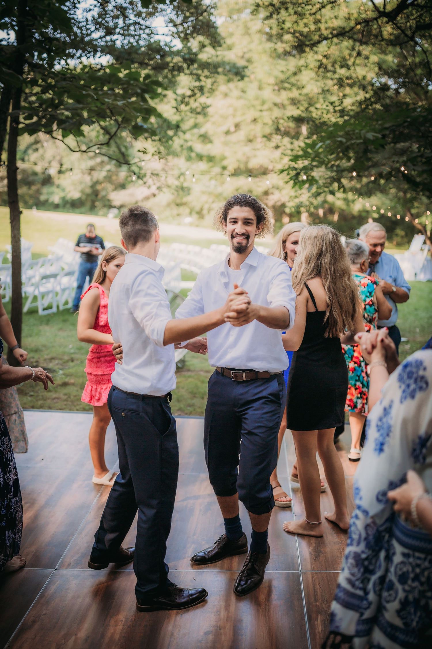 Wedding guests socializing and dancing on wooden deck at outdoor reception.