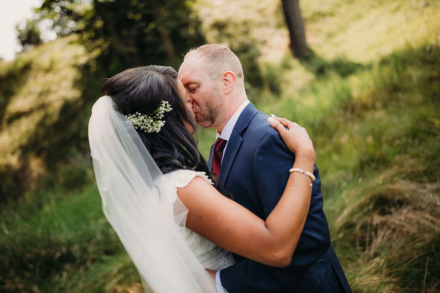 Intimate wedding moment captured between newlyweds in a sun-dappled forest setting.