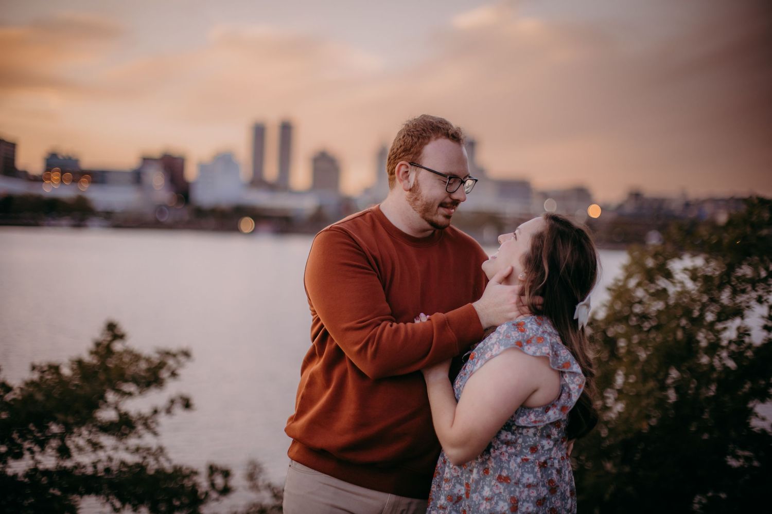Romantic sunset moment between couple with city skyline and water in background.