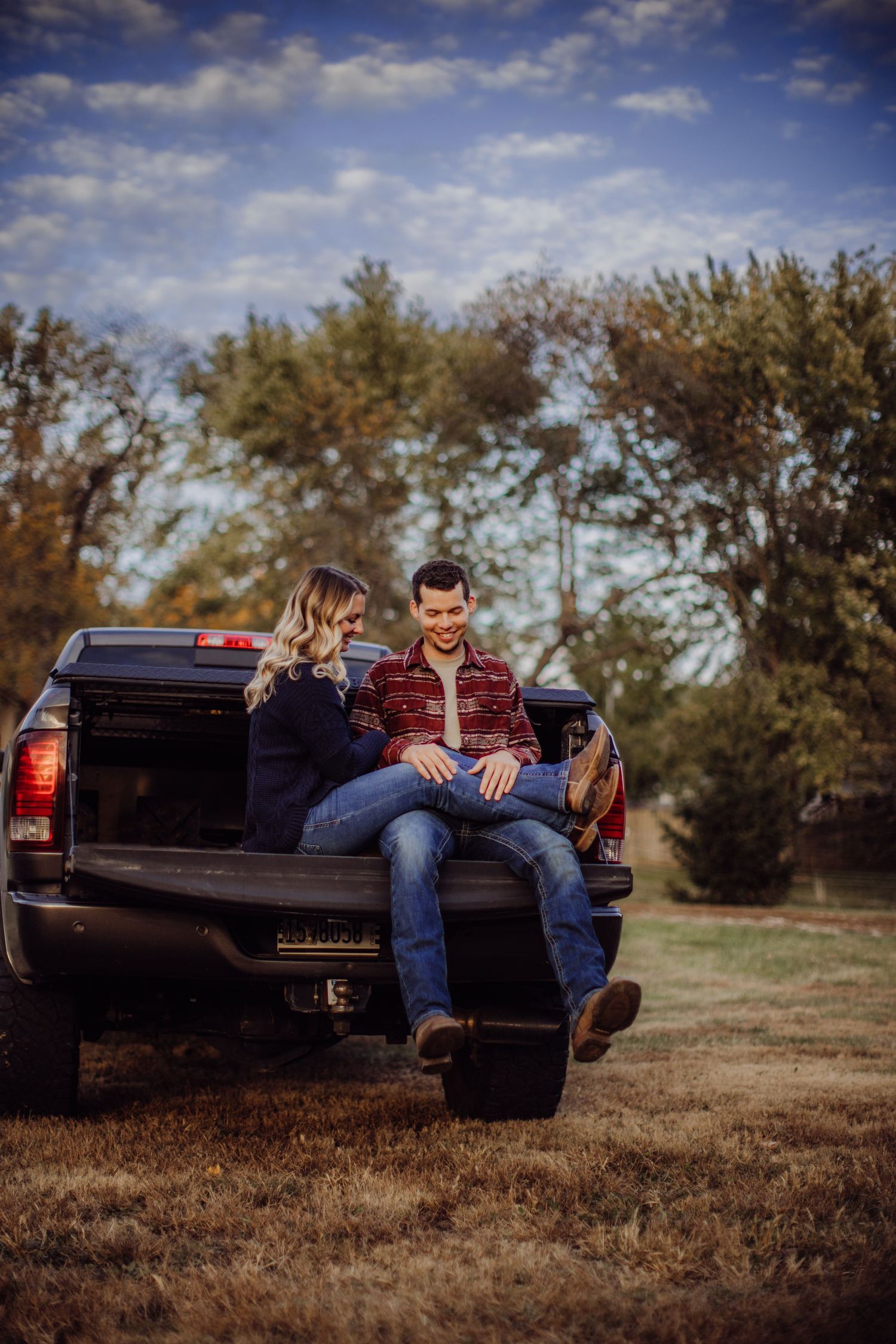 A couple relaxes together on the bed of a black pickup truck during a golden autumn afternoon.