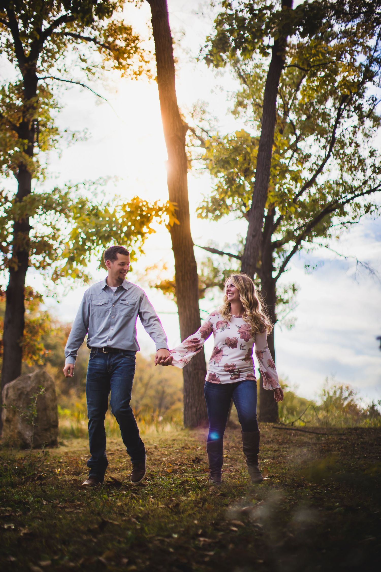 Couple holding hands while walking through a sunlit autumn forest.