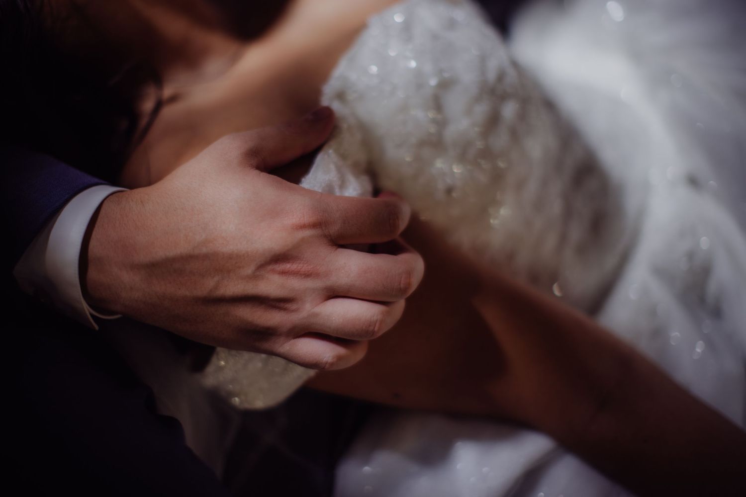 Artistic black and white detail shot of hands touching during a wedding moment.
