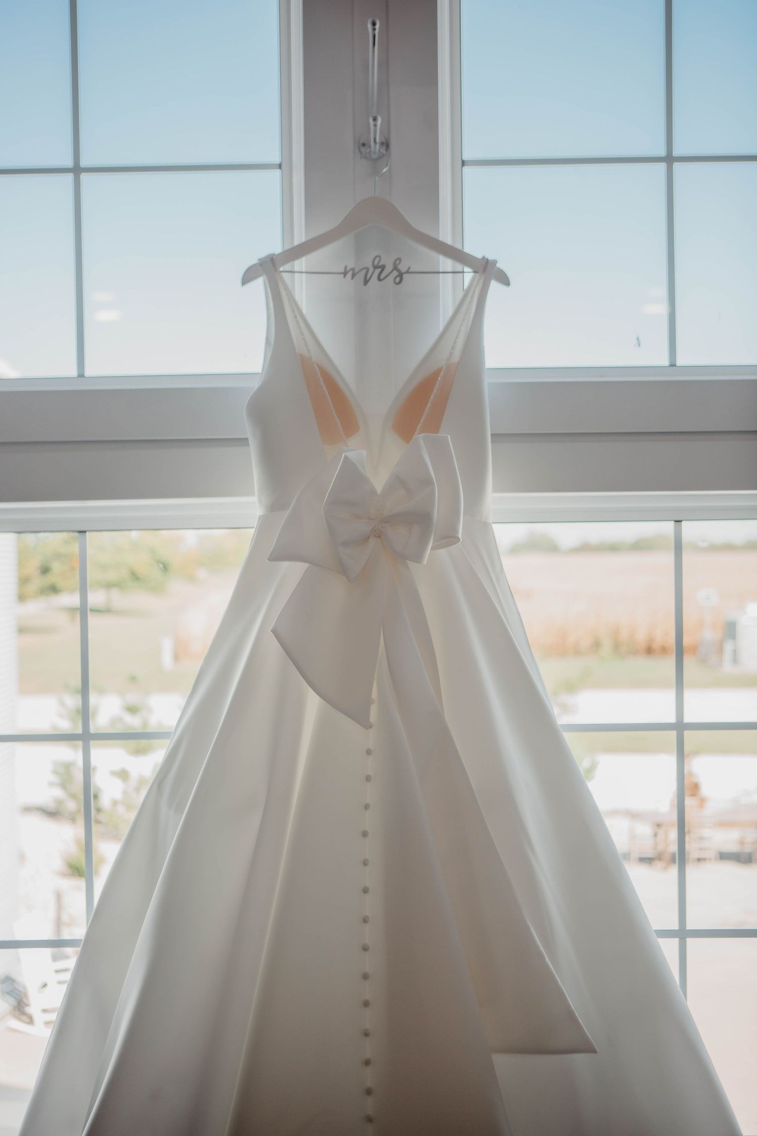 White wedding gown with button details and bow displayed against bright windows.