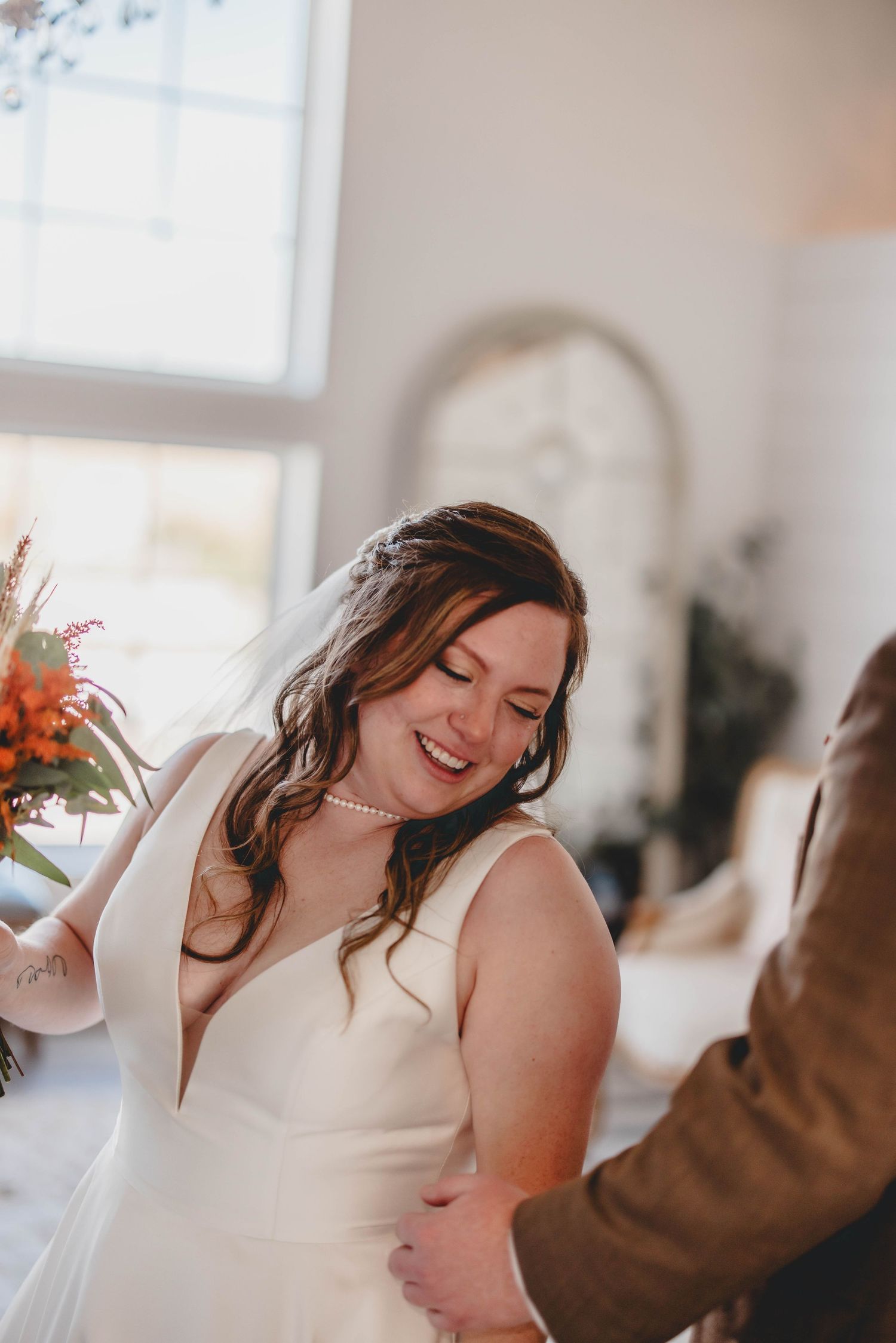 Candid laughter during wedding celebration with elegant white dress and autumn bouquet.