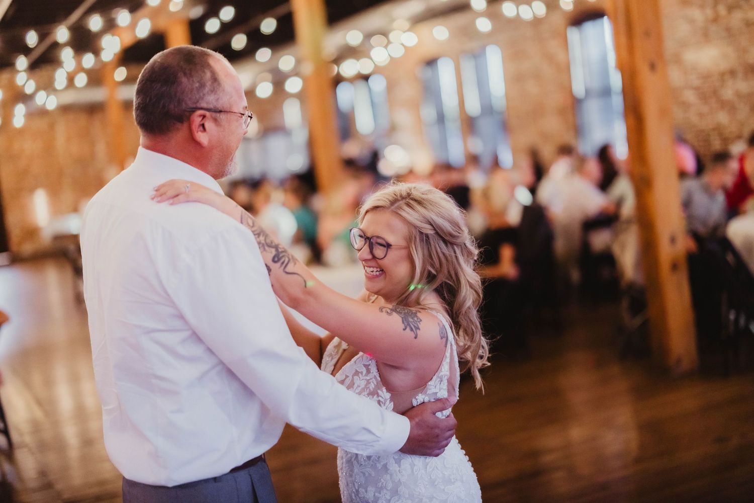 Intimate wedding dance moment captured in rustic venue with string lights overhead.