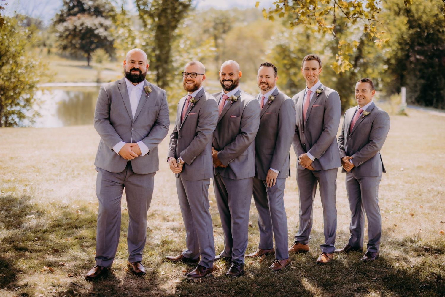 Wedding party lined up outdoors wearing coordinated grey suits and ties.