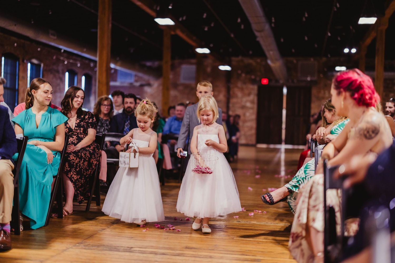 Wedding party members stand at the altar in front of exposed brick walls and tall windows.