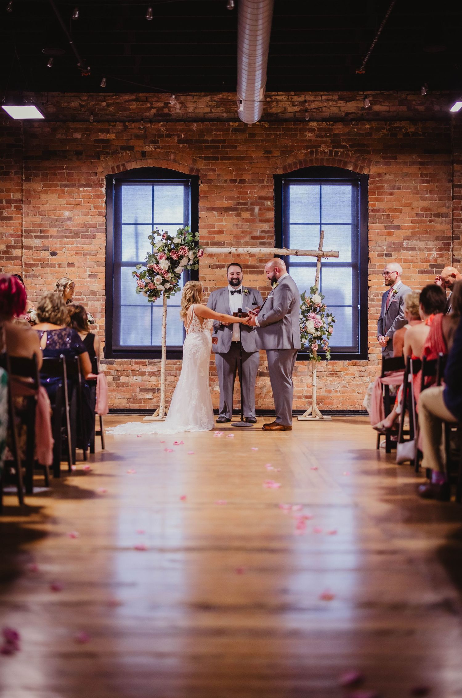 Wedding ceremony in industrial venue with exposed brick walls and floral arch decorations.