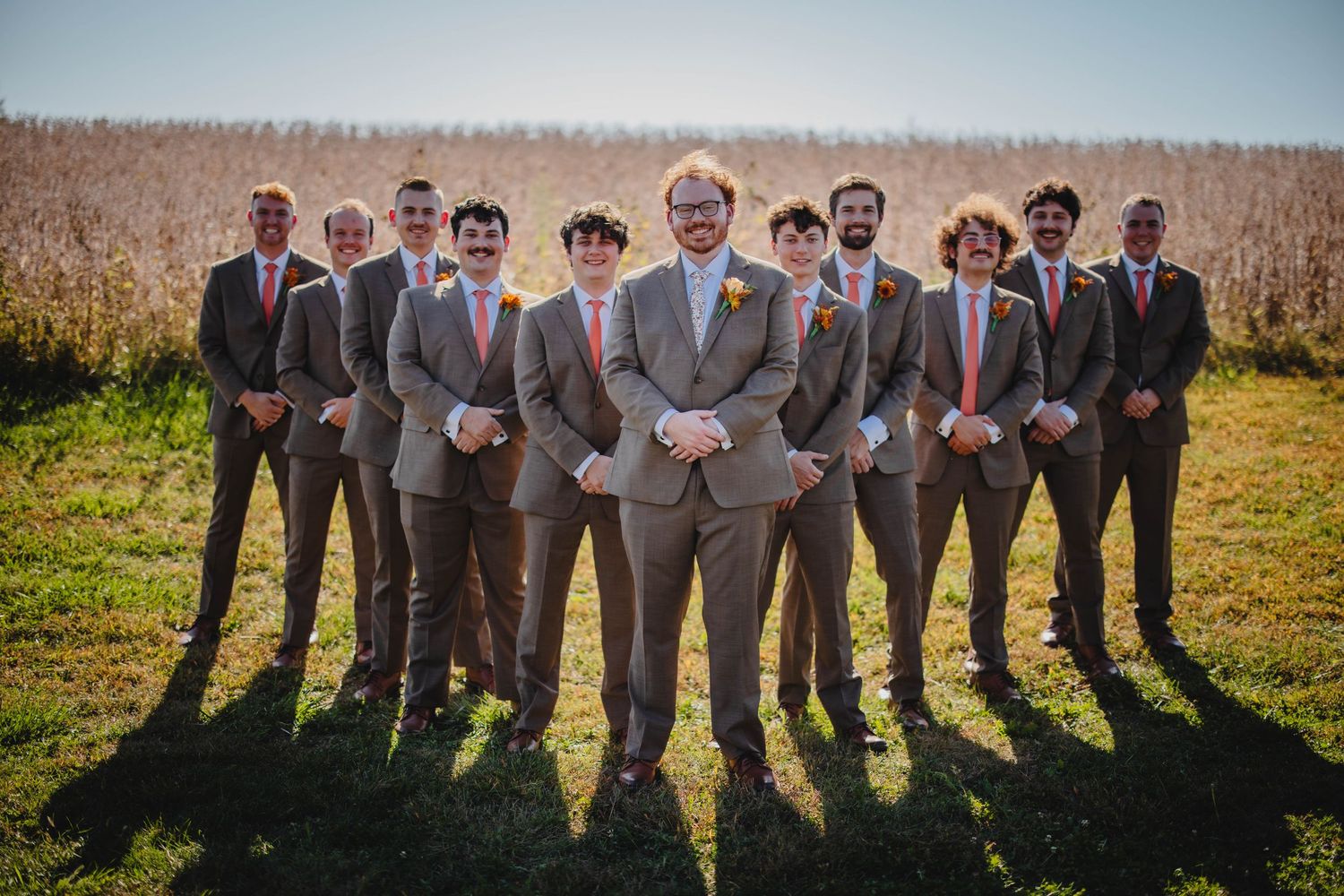 Groomsmen in gray suits pose together in front of cornfield.