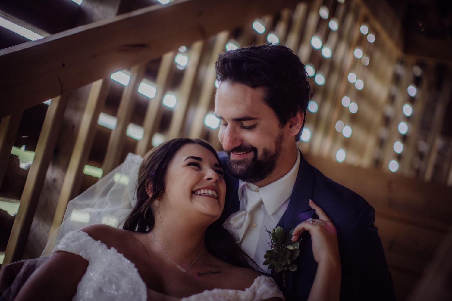 Joyful wedding moment captured on wooden staircase with twinkling lights behind.