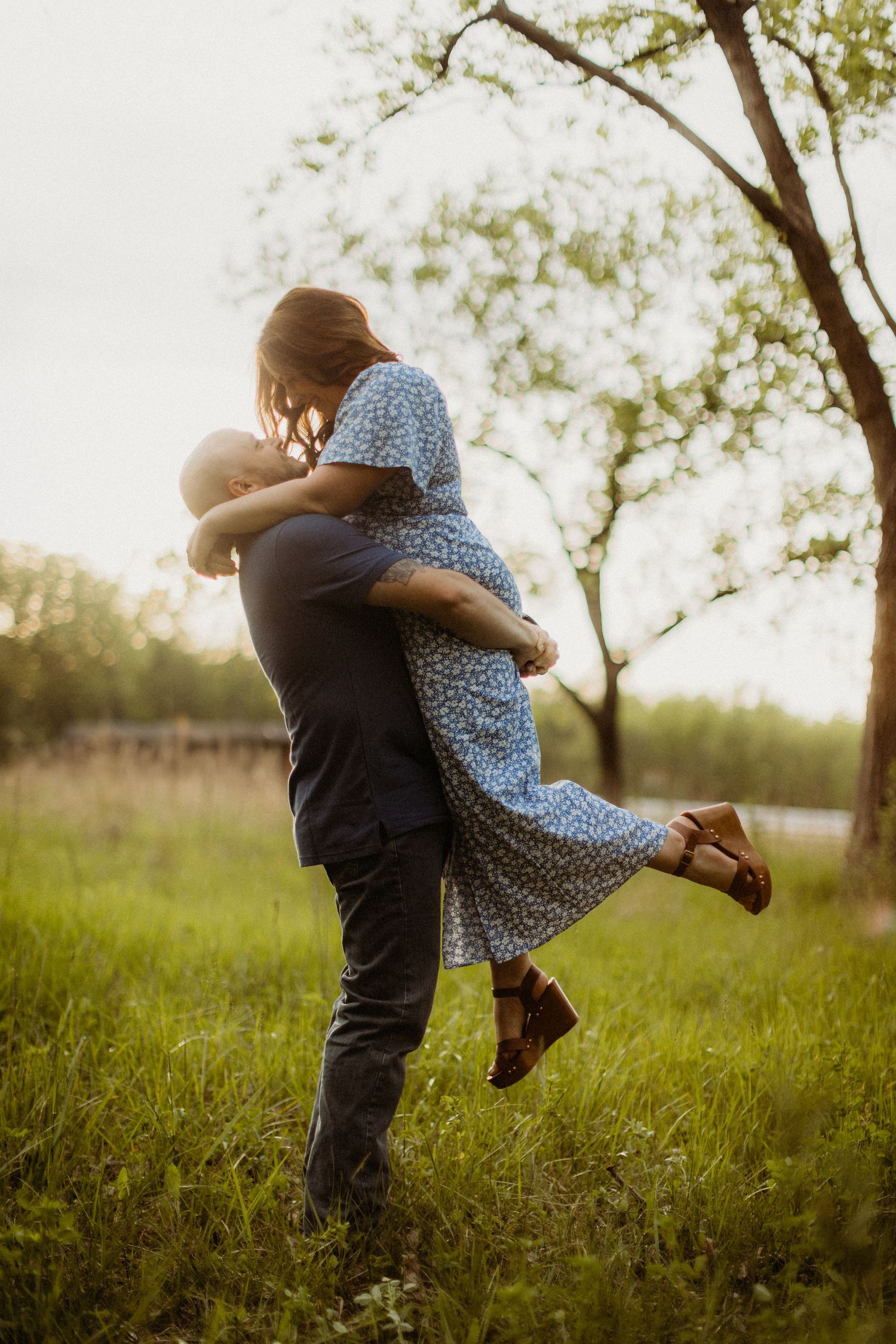 A romantic couple embraces in a grassy field at sunset as they share a tender moment together.