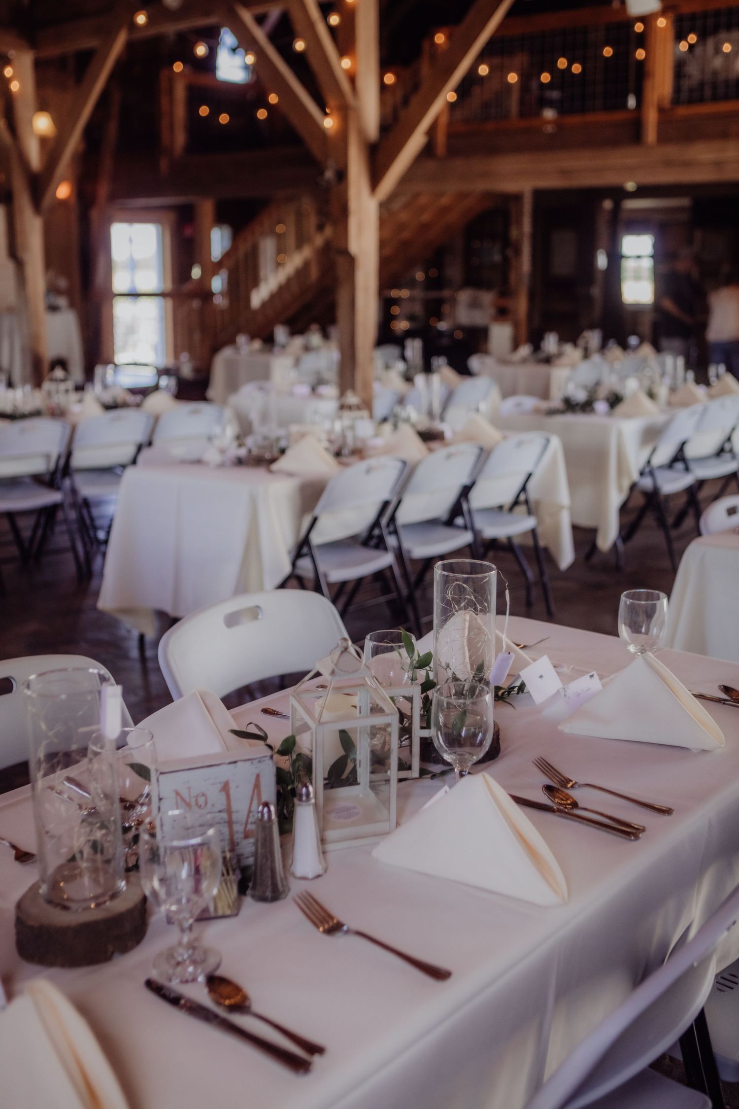 Rustic barn wedding reception with white tablecloths and string lights overhead.