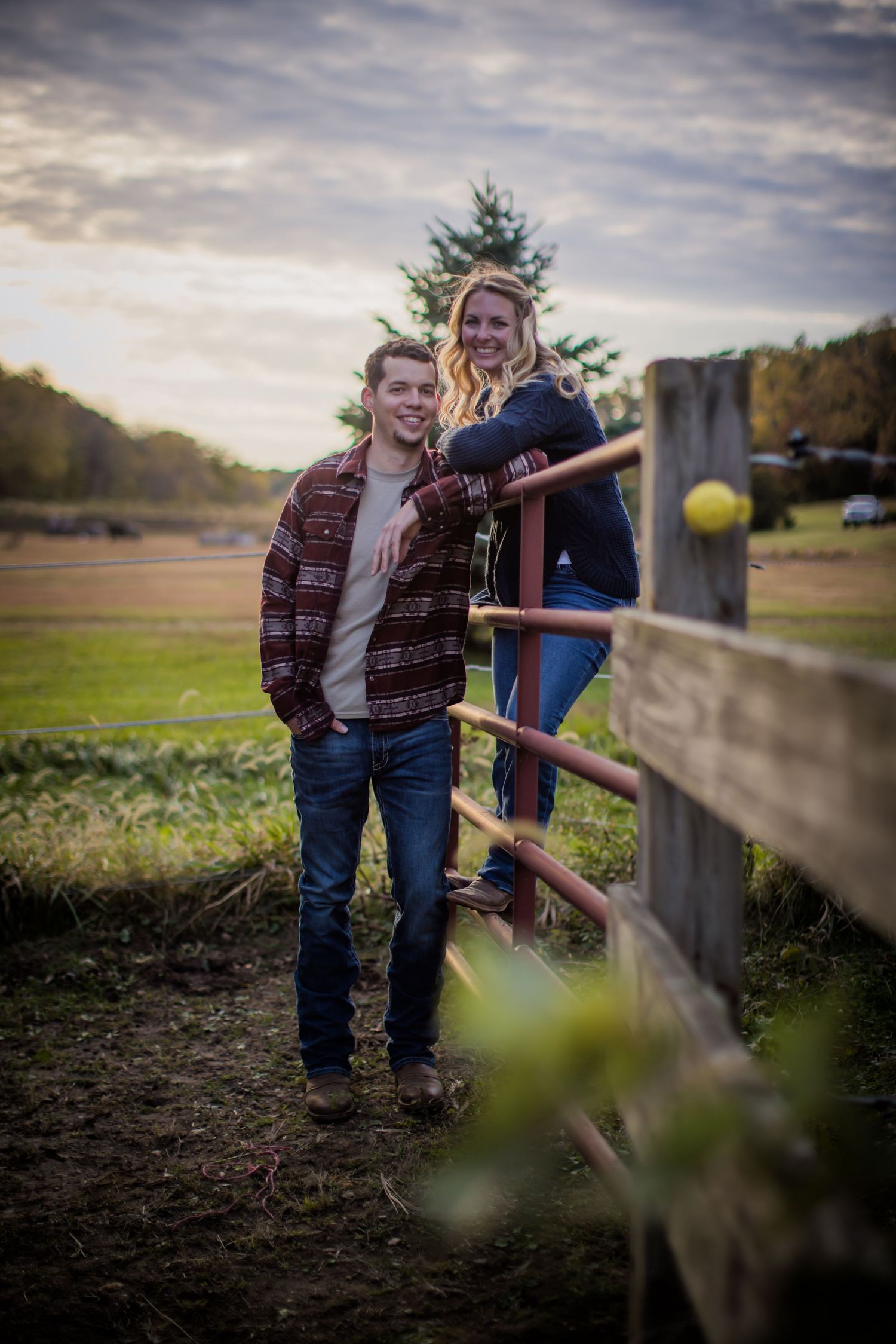 Couple poses by wooden fence during golden hour in autumn countryside.