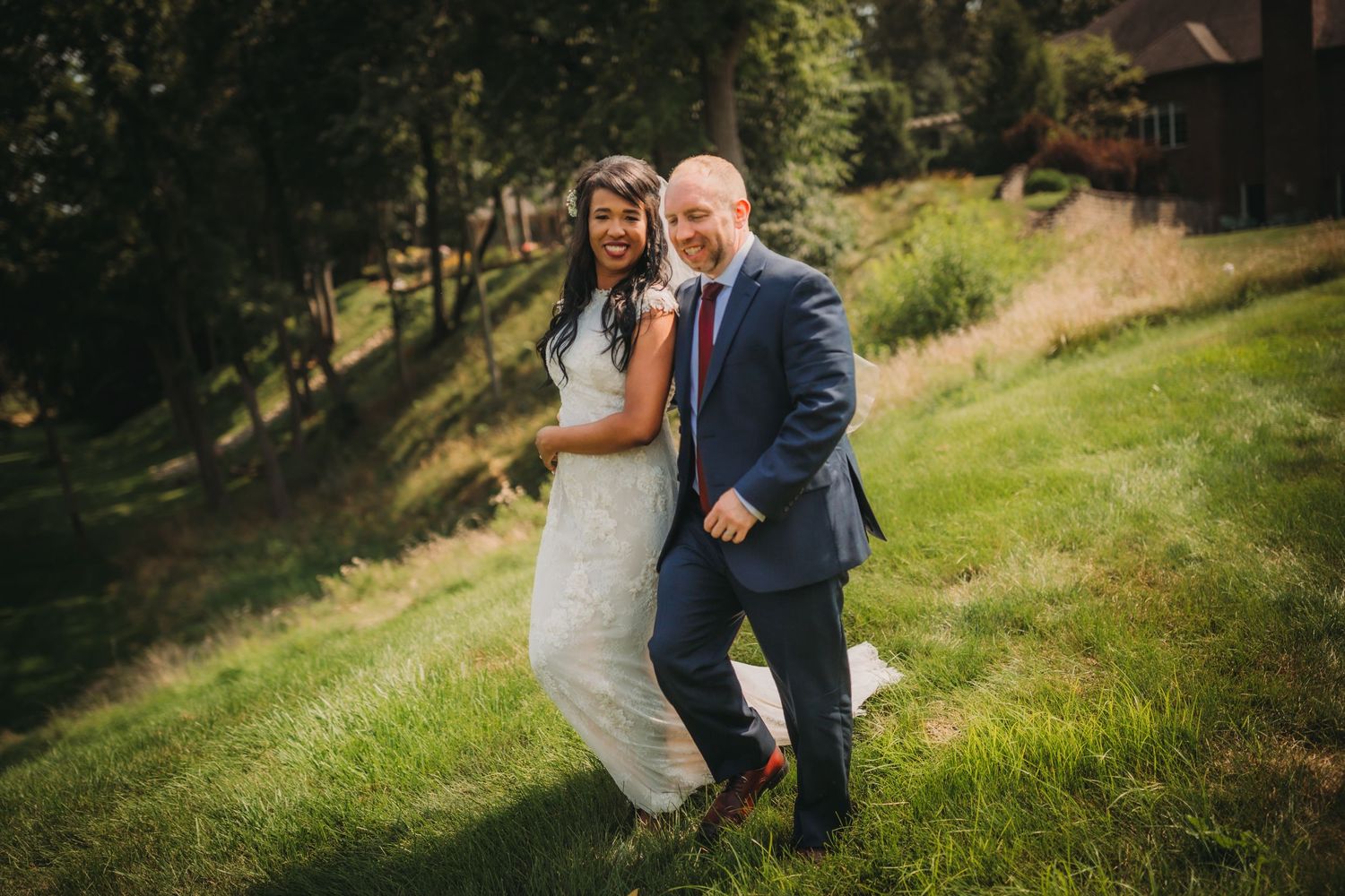 Couple shares a playful dance move on a grassy slope during their wedding.
