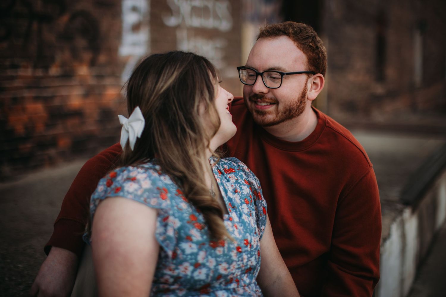 A loving couple embraces against an urban brick backdrop.