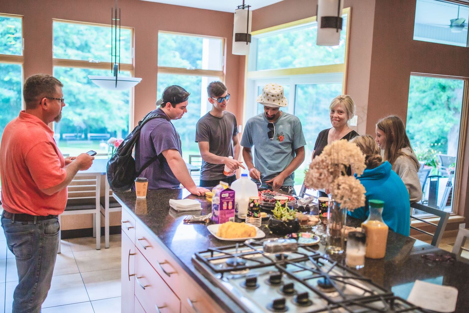 People gathered around kitchen counter sharing food and conversation at casual event.